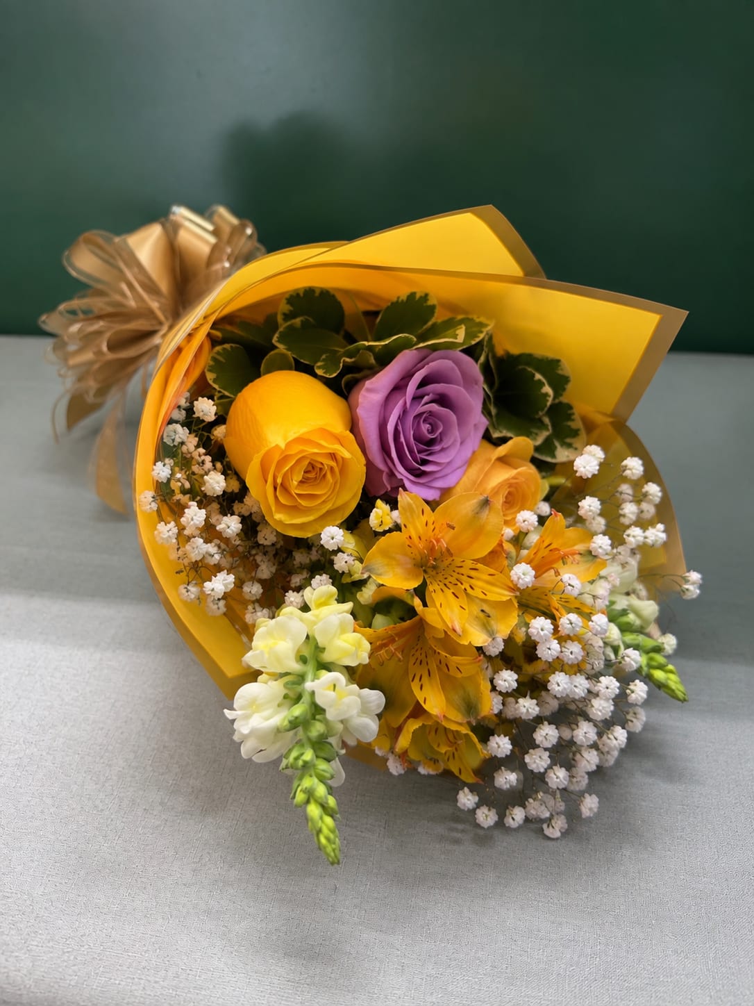 Bouquet of yellow, purple, and orange flowers wrapped in gold paper