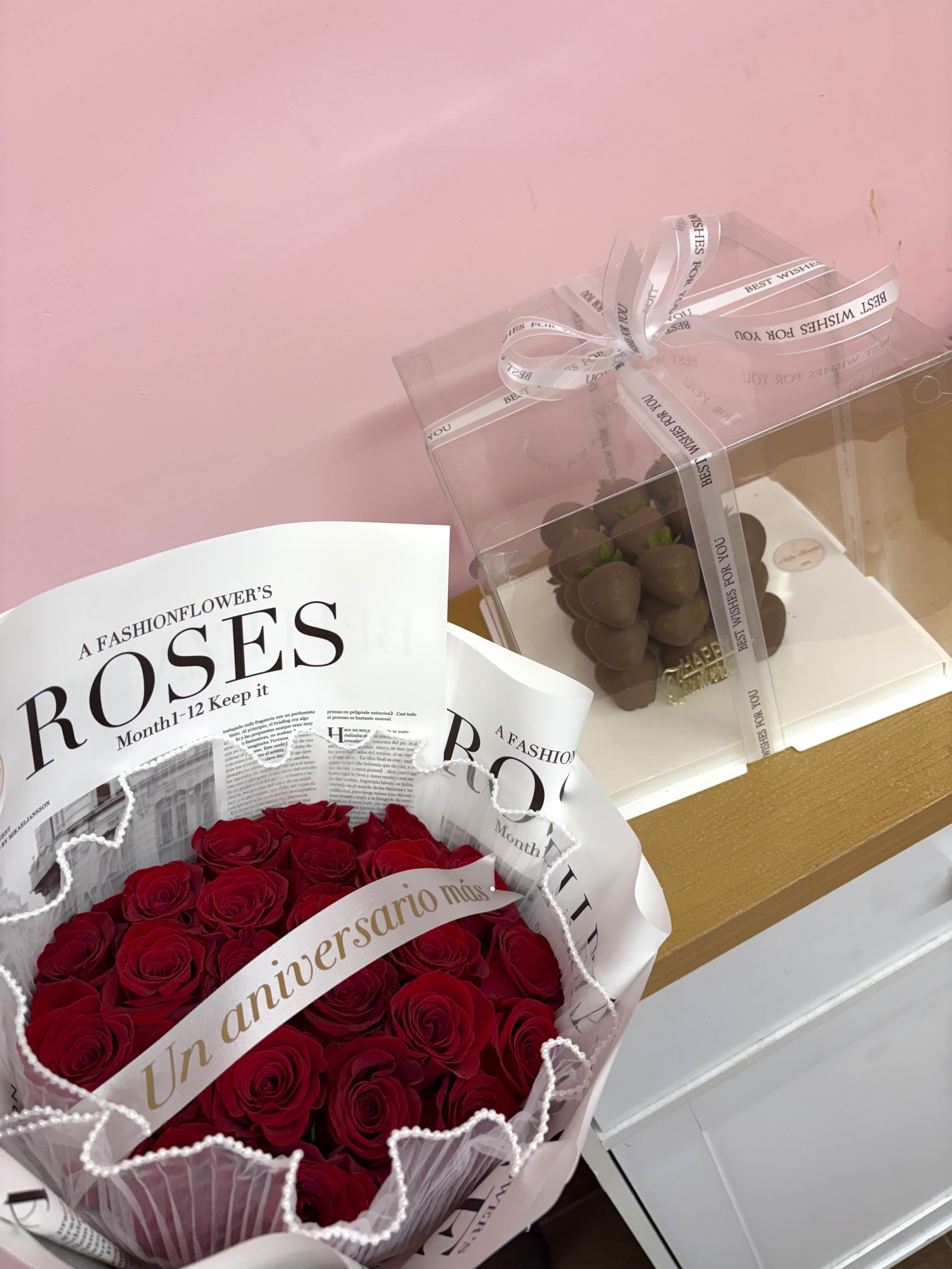 Bouquet of red roses in pink and white wrapping beside a clear gift box of chocolates