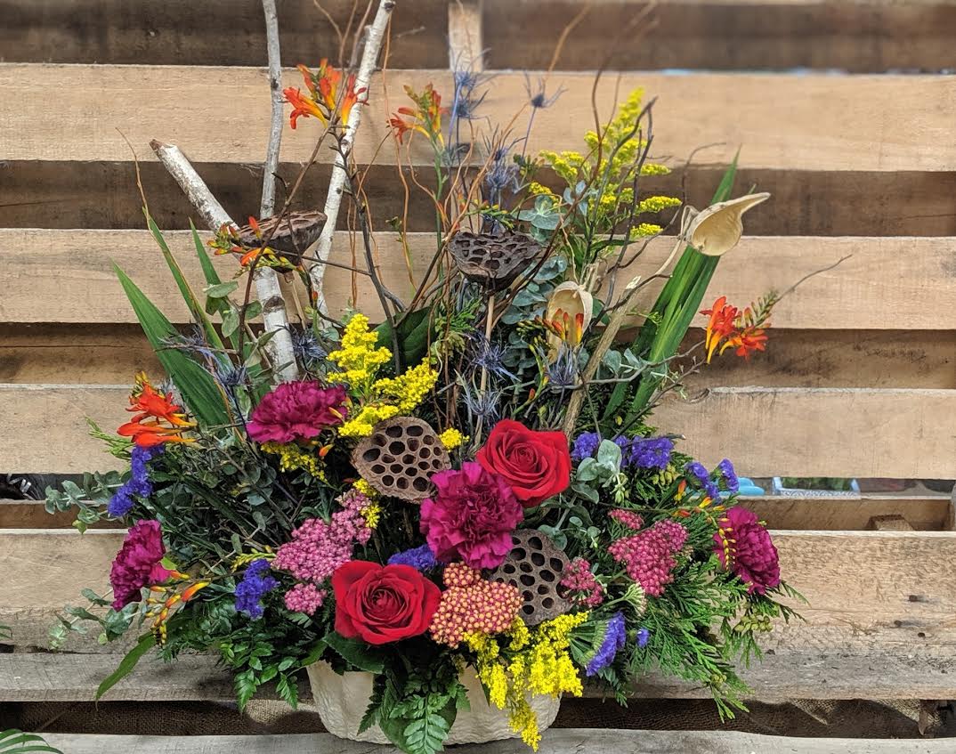 Colorful mixed floral arrangement with roses and calla lilies in a container