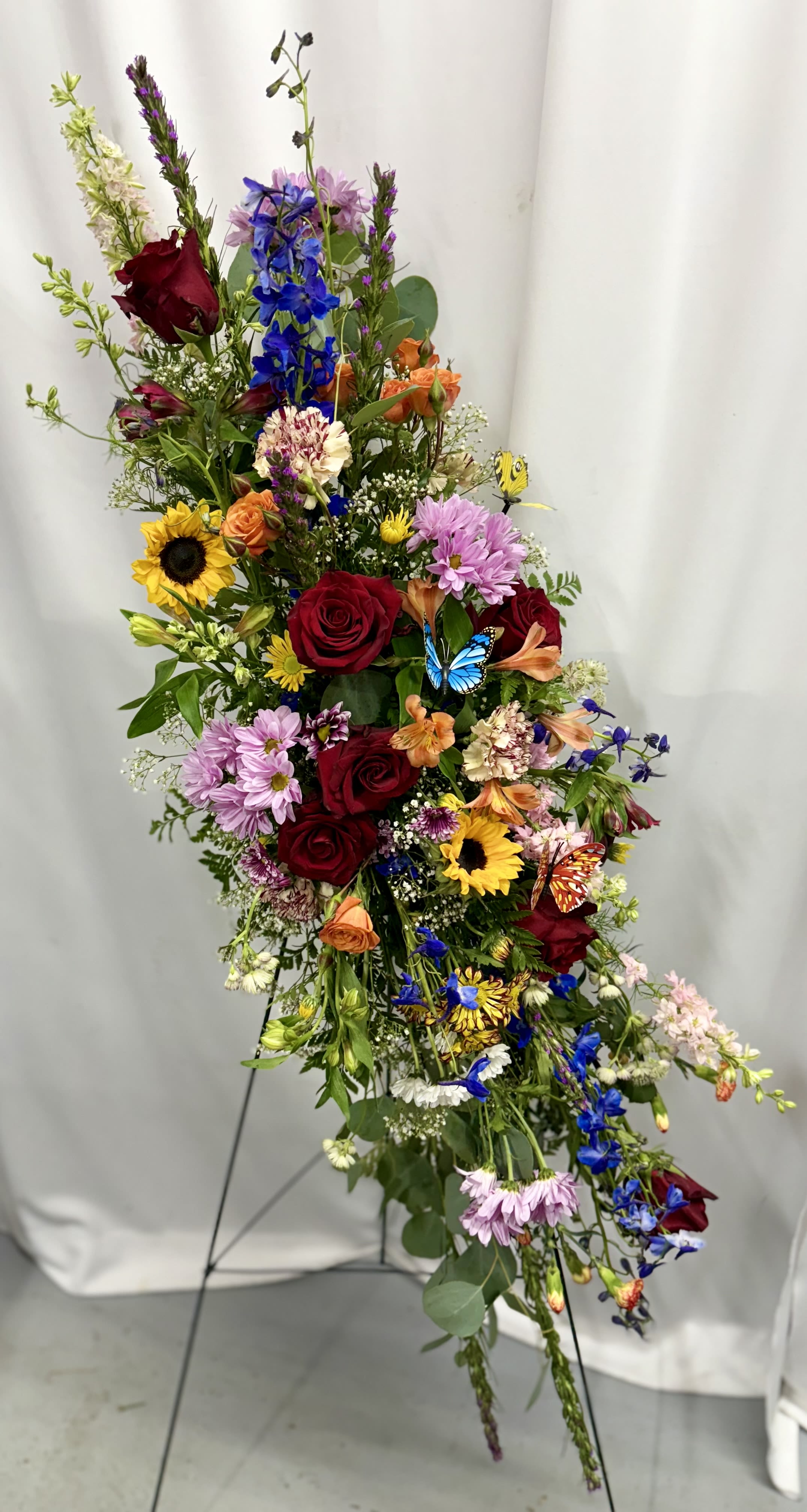 Tall mixed flower arrangement with roses, sunflowers, and blue blooms