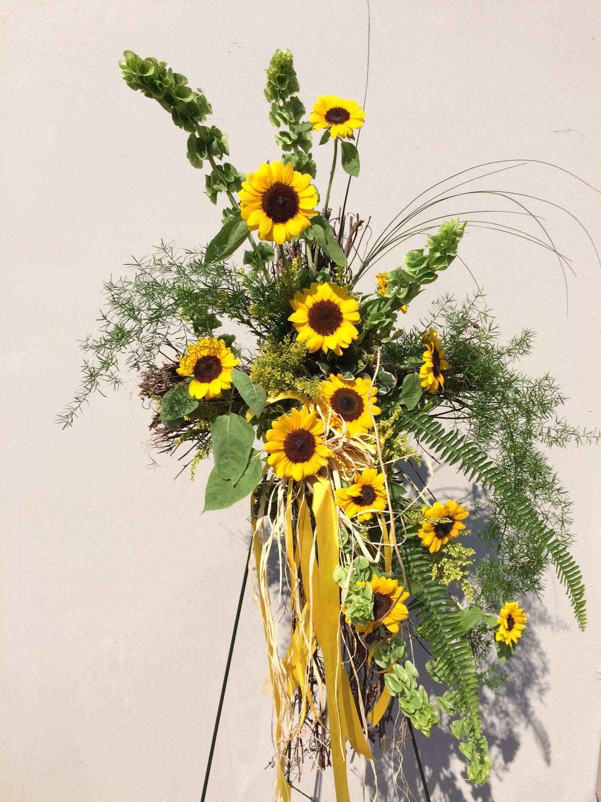 Tall sunflower arrangement with yellow ribbons and greenery on a stand