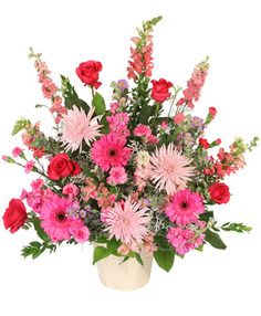 Pink and red mixed flower arrangement in a cream vase
