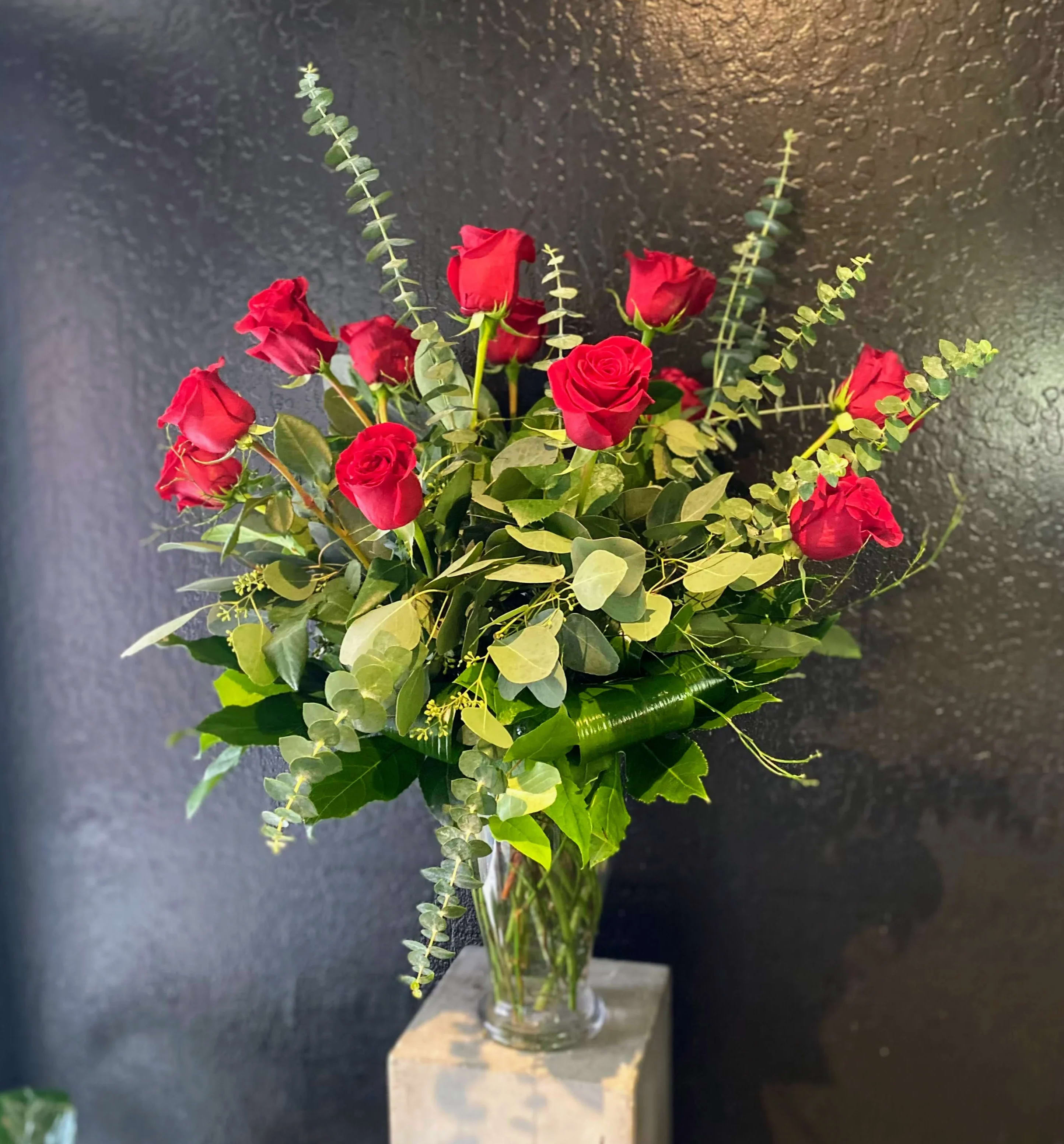 Red roses arranged in a clear glass vase with eucalyptus foliage