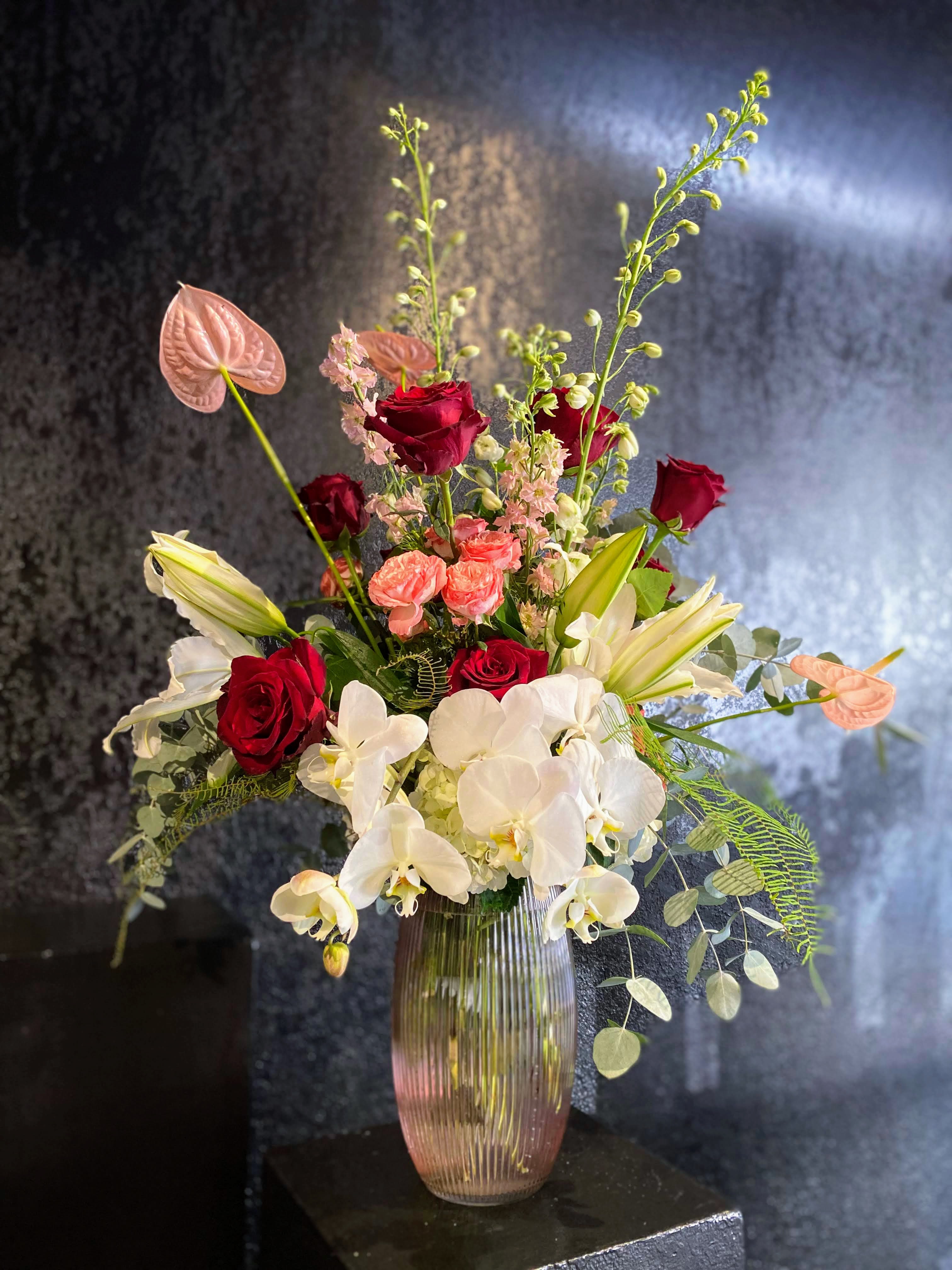 Mixed bouquet of red roses, white orchids, and lilies in a glass vase