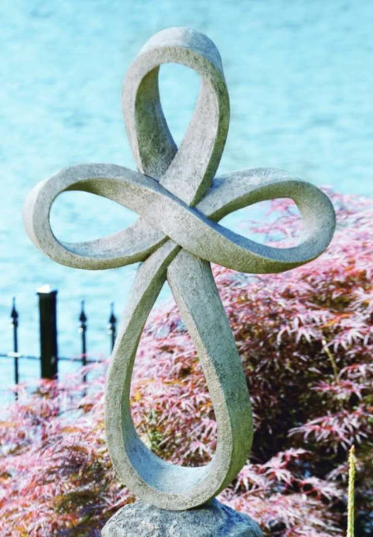 Stone sculpture with interlocking loops beside a pond and pink shrubs