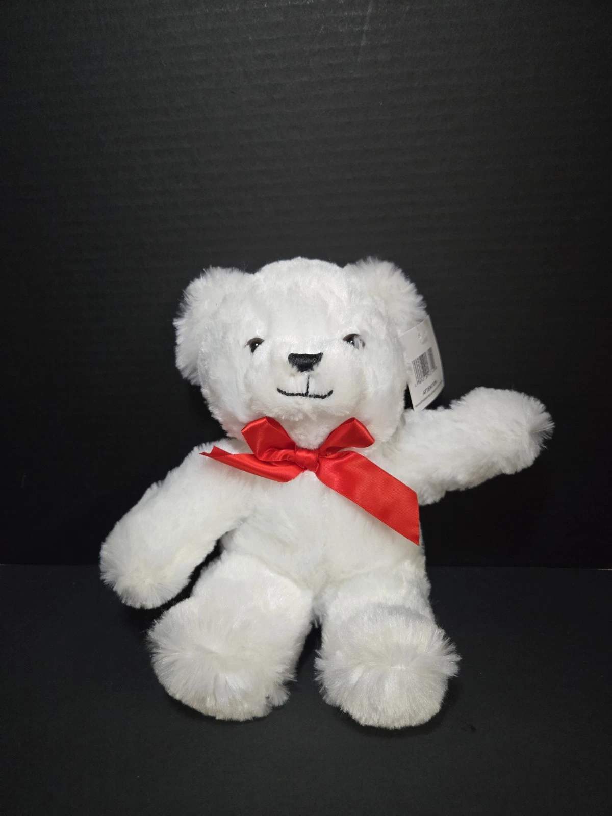 White teddy bear with a red ribbon bow on a black background