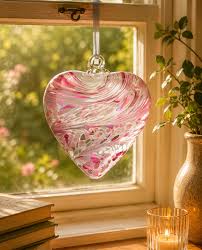 Heart-shaped pink and white glass ornament hanging in a window