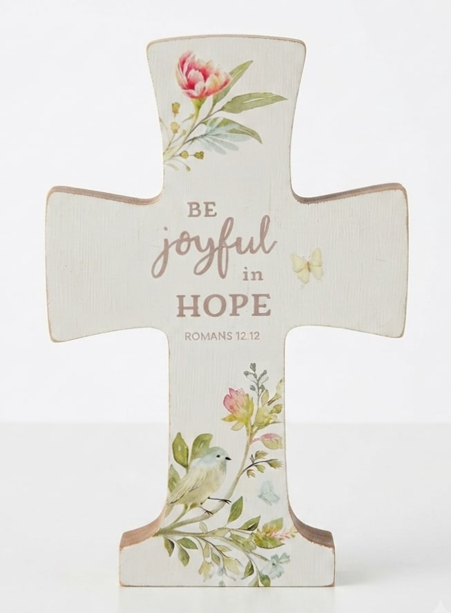 Cross-shaped decorative sign with floral print and the words "Be joyful in hope"