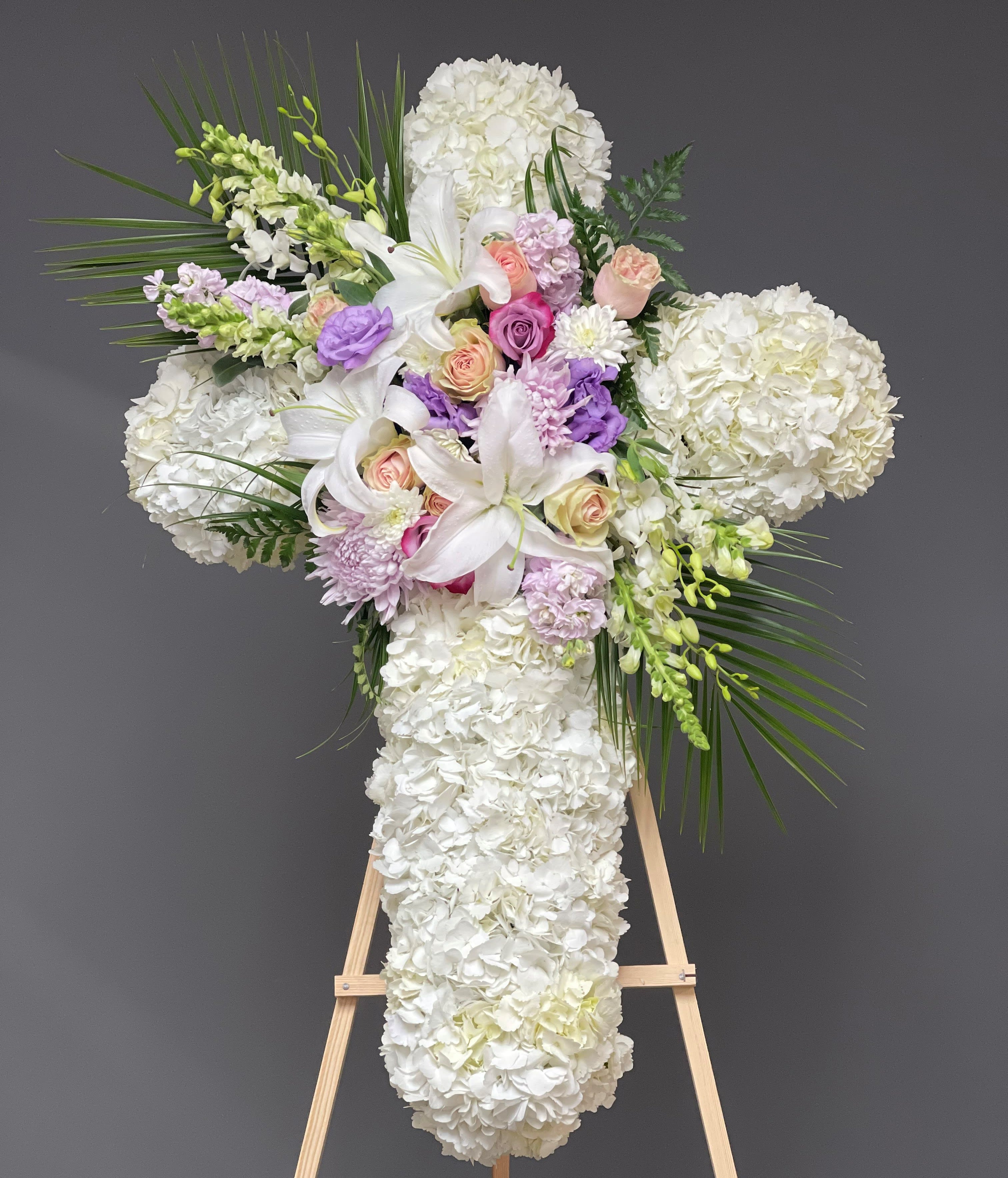 White floral cross arrangement with lilies, roses, and hydrangeas on an easel
