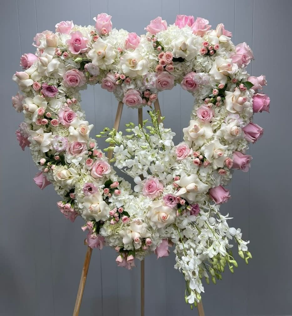 Heart-shaped floral wreath with pink and white roses and orchids on an easel