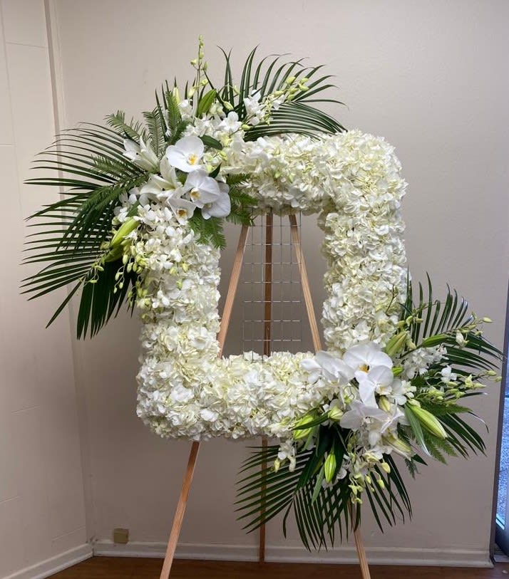 Large white floral wreath on an easel with palm fronds and orchids