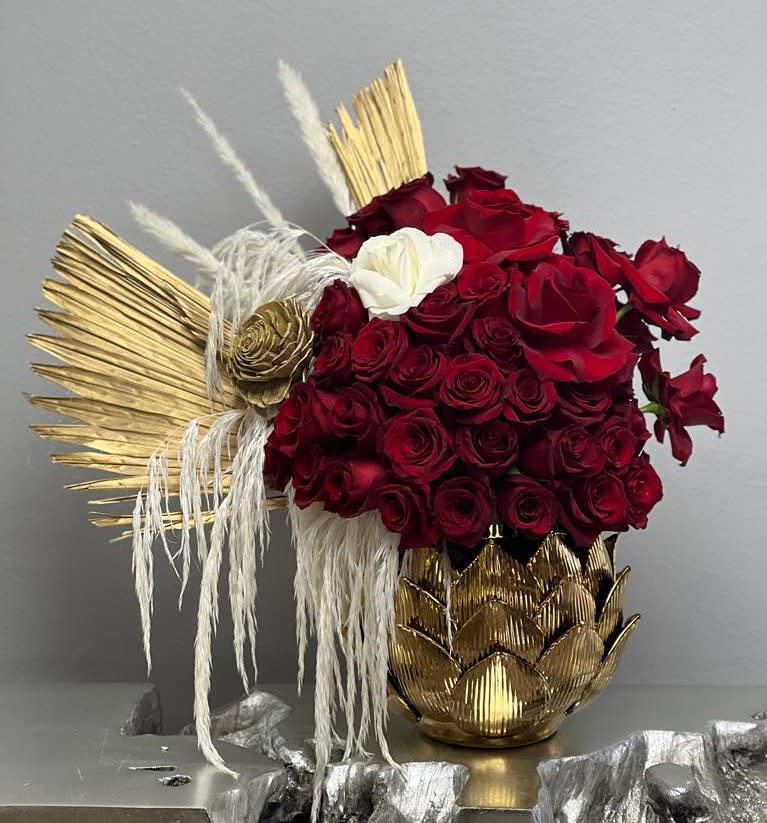 Red roses arranged with gold decorative accents in a gold vase