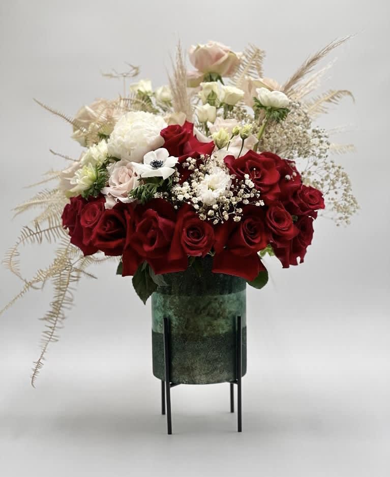 Red and white rose arrangement in a green vase on a stand