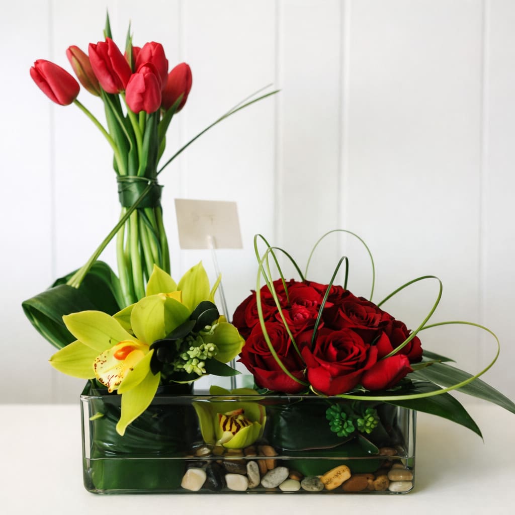 Red tulips and roses arranged in a glass vase with yellow orchids
