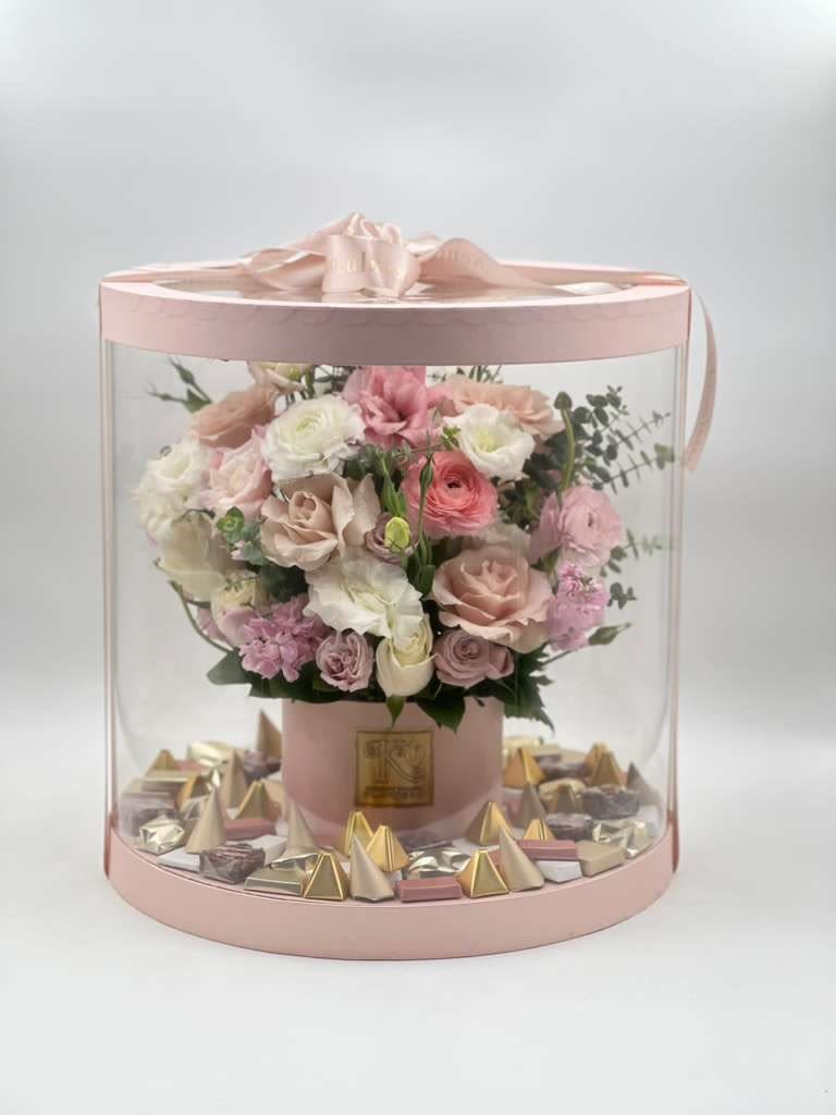 Love in Bloom &amp; Chocolate - A luxurious floral and chocolate creation designed to impress, this arrangement features a delicate palette of blush, ivory, and soft pink flowers beautifully arranged in a signature hat box and enclosed in a clear round presentation case. Finished with premium assorted chocolates at the base, it is a sophisticated gift that combines fresh floral beauty with sweet indulgence. Perfect for birthdays, anniversaries, baby celebrations, thank-you gifts, or simply to make someone feel cherished, this design brings together fresh flowers and sweet indulgence in one stunning presentation.