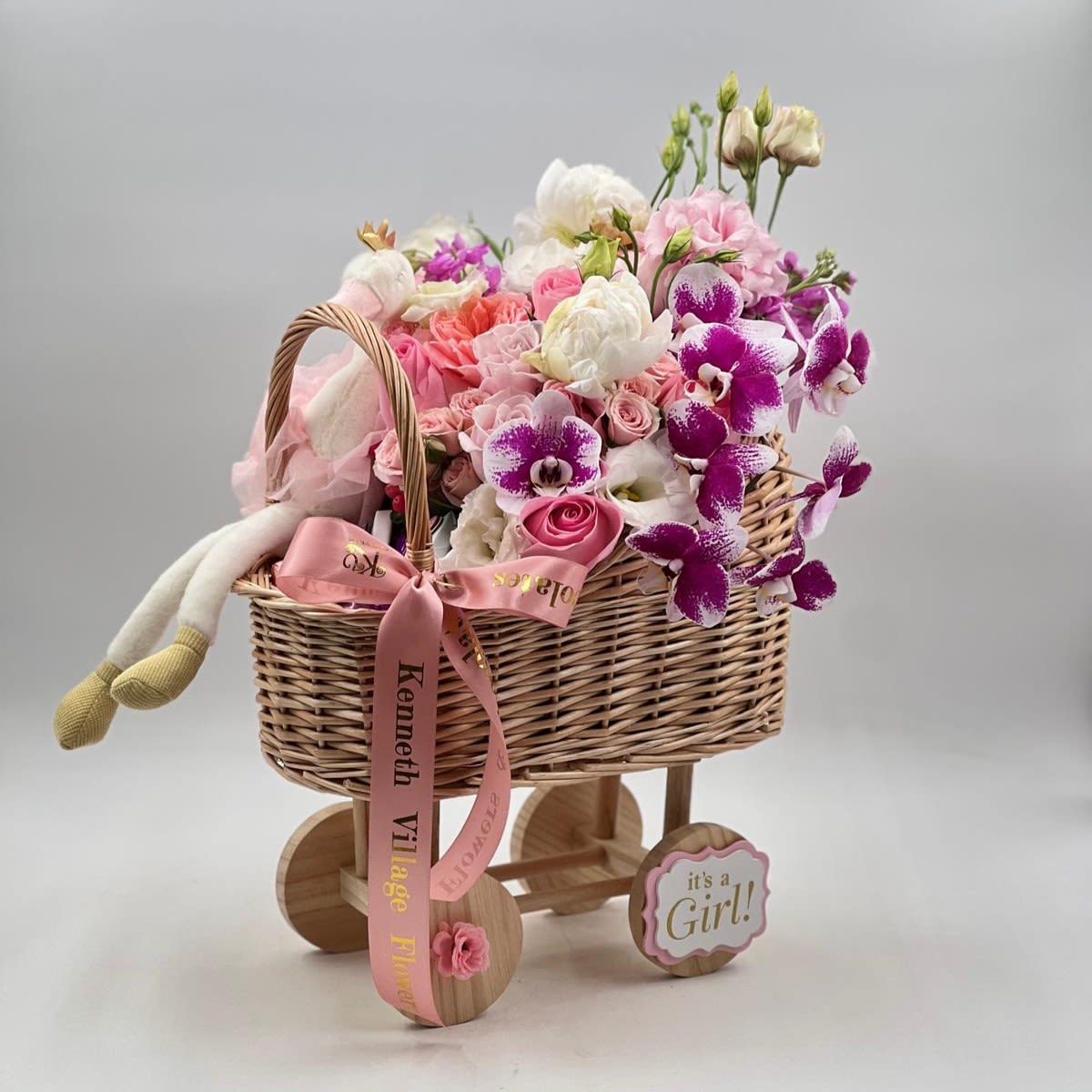 Sweet Baby Girl Basket - A charming baby girl gift arrangement designed in a stroller basket, filled with soft pink and white blooms, roses, orchids, and delicate seasonal flowers. Finished with a plush bunny and elegant ribbon, this sweet design is perfect for welcoming a newborn baby girl or celebrating a baby shower.