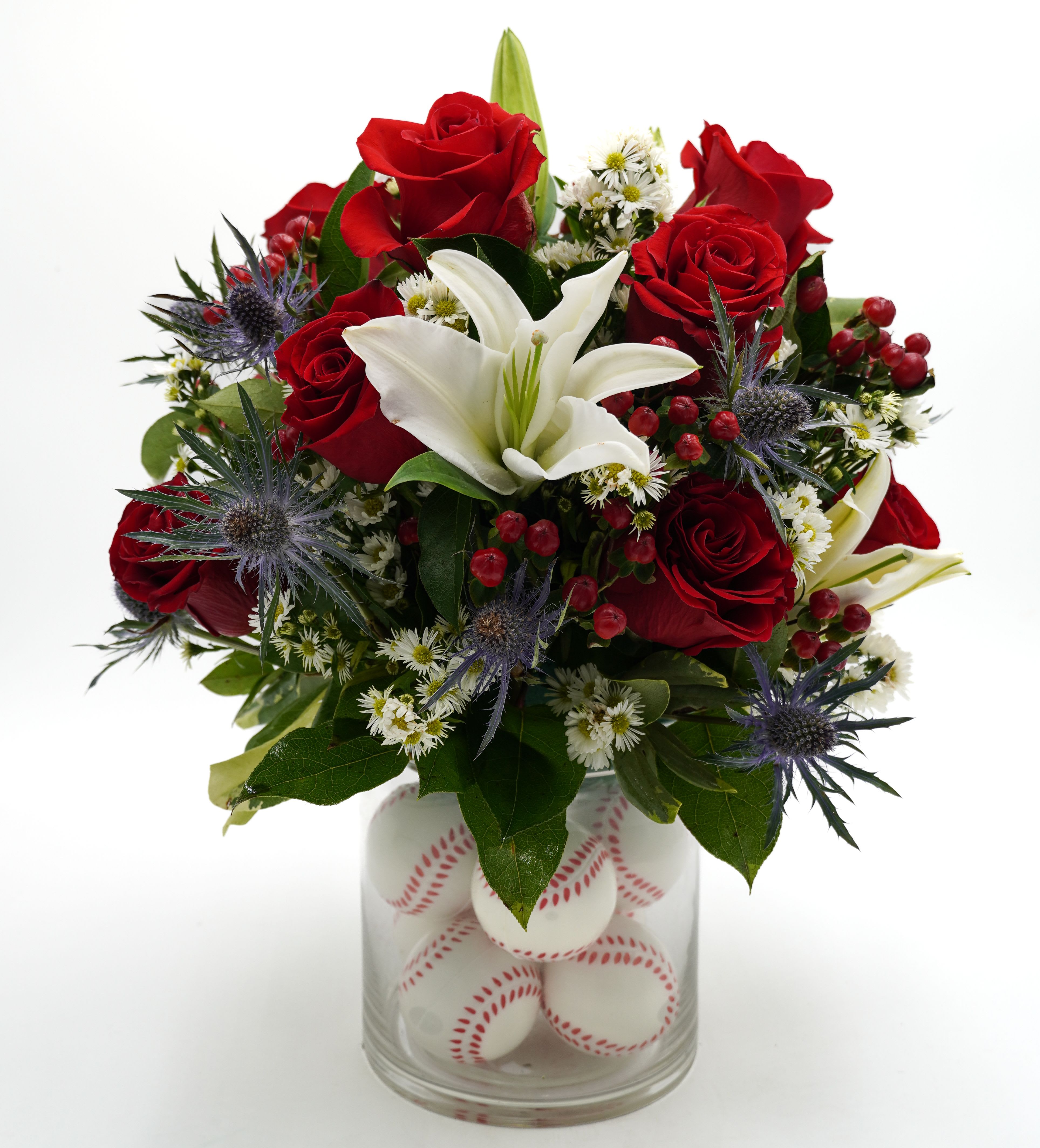 Red roses and a white lily in a glass vase filled with baseballs