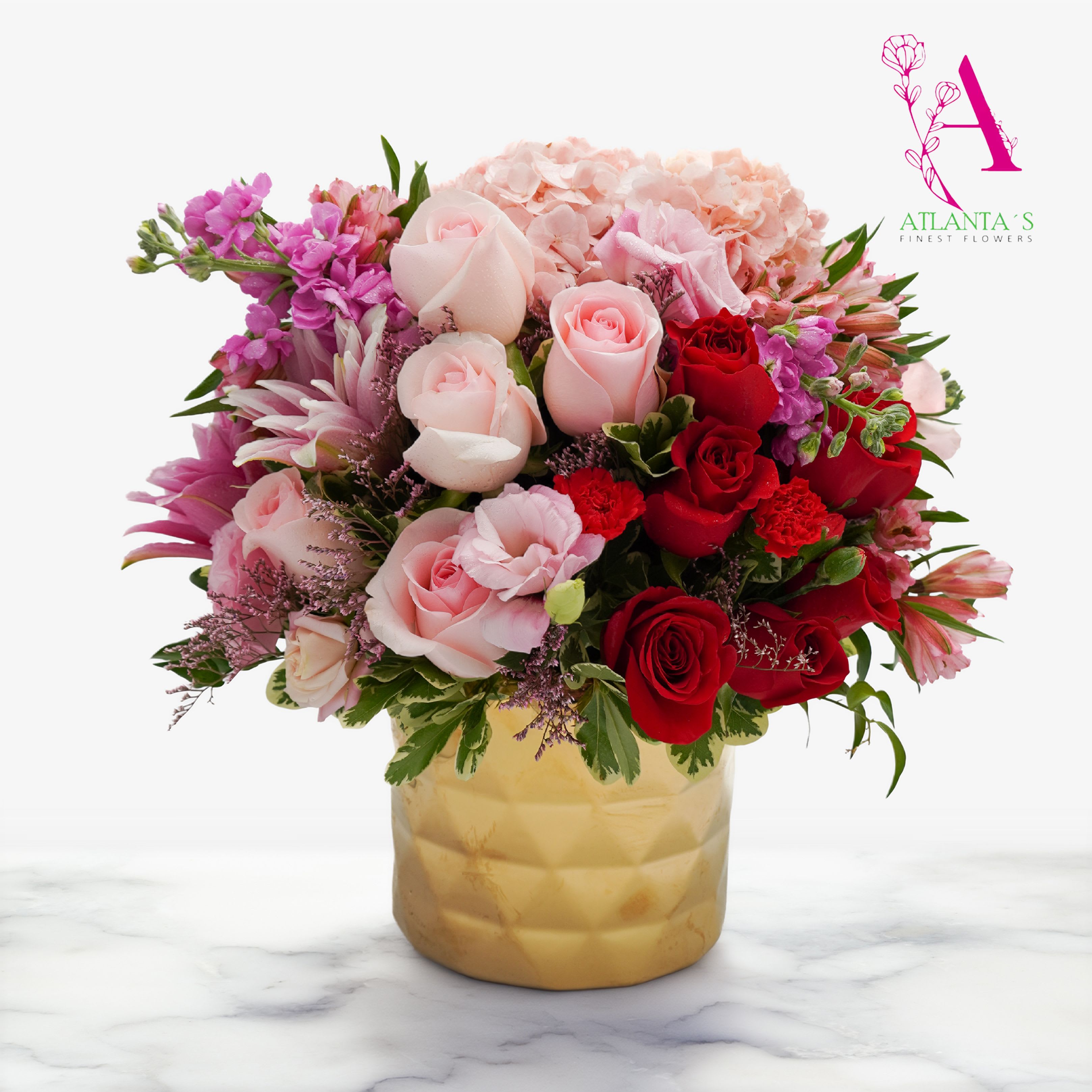 Arrive in style by Atlantas Finest Flowers  - A lush, rounded centerpiece that reads as romance and celebration in equal measure - perfect as an anniversary bouquet or a birthday surprise. This flower arrangement for anniversary, love and romance, or "just because" moments mixes soft blush and white lilies with vivid red and pink roses to create an immediate emotional impact; she'll feel truly celebrated the moment the gold vase arrives at her door.  Generous pale hydrangea and sprays of alstroemeria and spray roses give the design its full, layered silhouette, while small purple stock-like fillers add delicate contrast and texture. The arrangement is arranged densely and outward for an abundant, centerpiece-style look; the polished gold vase elevates the composition for special occasions like Mother's Day, Women's Day, Best Friends Day, or Admin Professionals' Week - and it still reads fresh for spring, Easter, or a thoughtful get-well or "I'm sorry" gesture.  This is a large, statement arrangement intended to be the room's focal point-ideal for congratulating someone, honoring a grandparent, or marking Valentine's Day or Breast Cancer Awareness Month with pink tones. For best longevity, place away from direct heat and drafts and refresh the vase water every few days so the lilies, hydrangeas, roses, and alstroemeria stay vibrant.