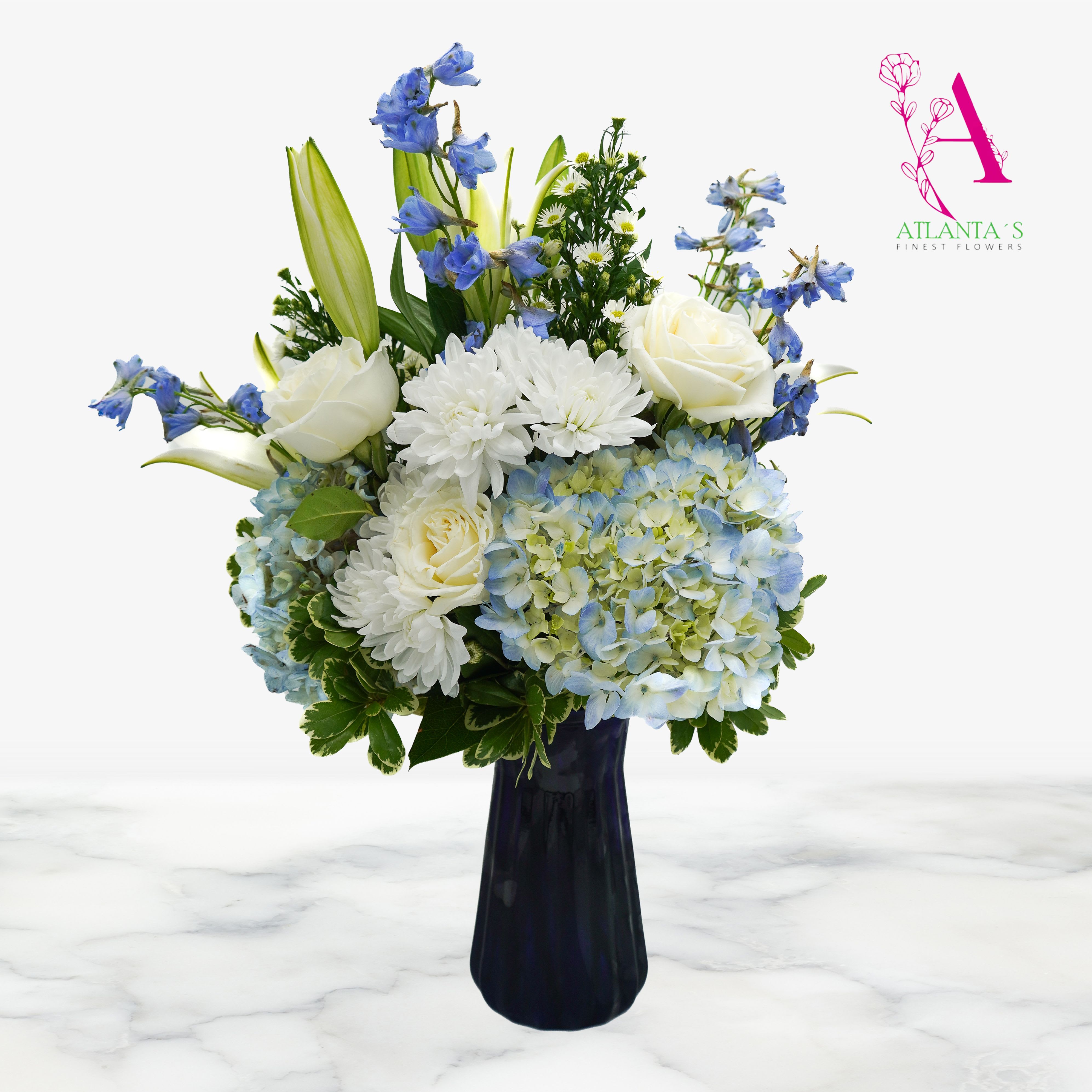 Sky Blue Bouquet - Celebrate Mom with this elegant Mother’s Day arrangement featuring a stunning blue vase filled with lush blue hydrangeas, accented by a mix of white and blue blooms and greenery. This fresh floral piece brings a calming and graceful touch to any space. A perfect way to show love and appreciation on her special day.  Vase Size: 9"H x 5"W 