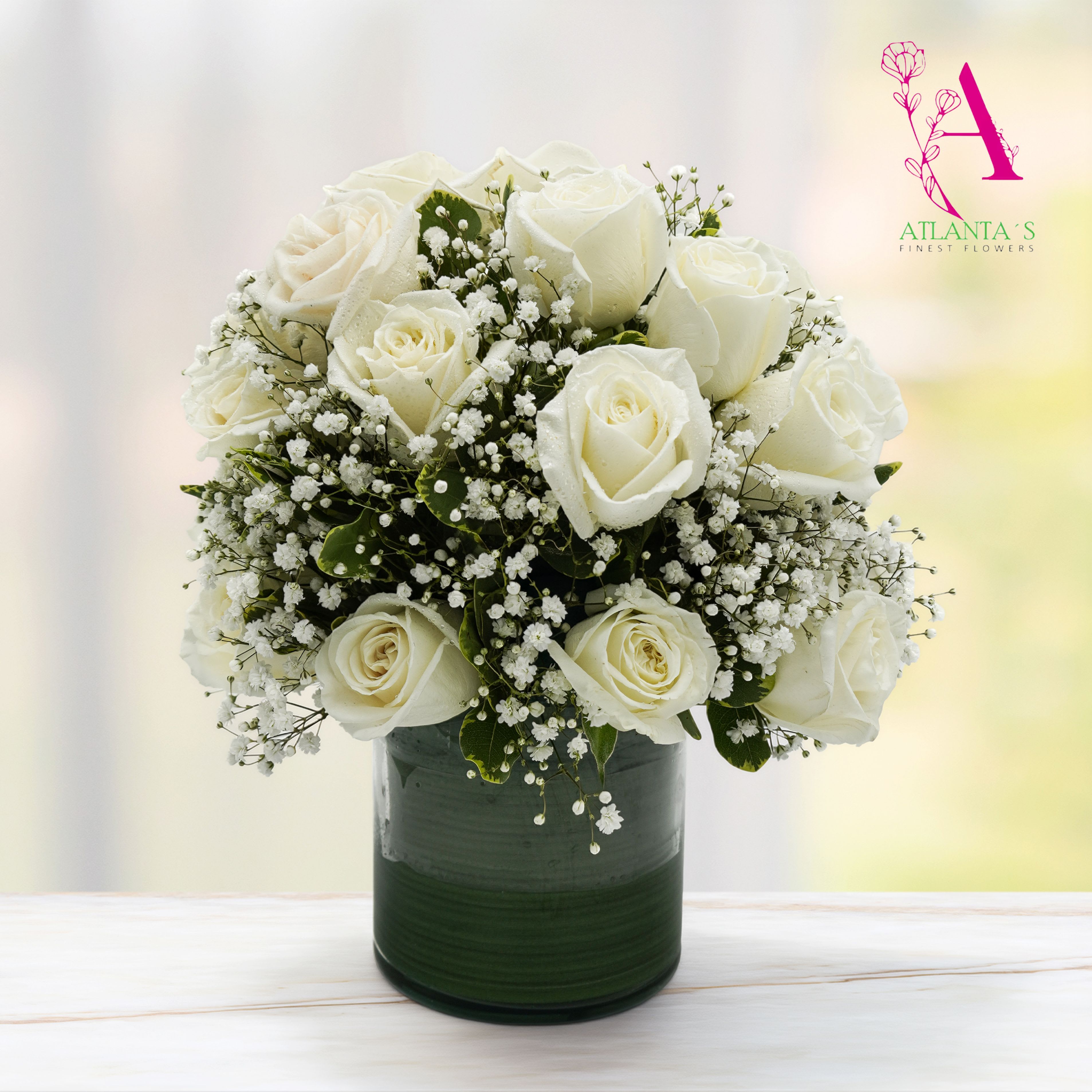 Heavenly White  - An arrangement of elegant white roses surrounded by baby’s breath and lush greenery, beautifully designed in a modern glass vase. This classic piece symbolizes peace, purity, and remembrance, making it a heartfelt expression of sympathy.