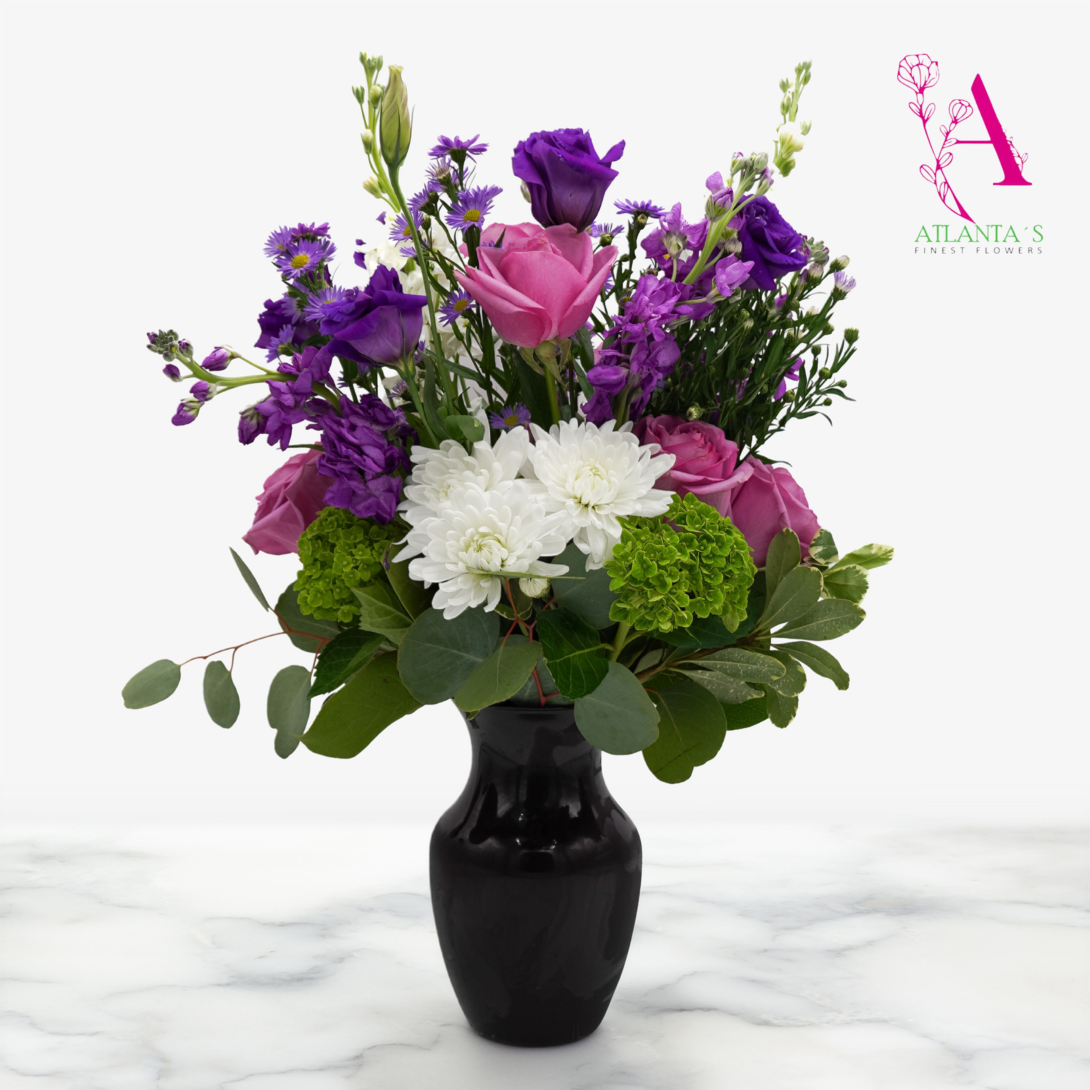 Enchanted Violet - A graceful blend of lavender roses, vibrant purple blooms, and soft white chrysanthemums, accented with fresh greenery and arranged in a purple vase. This elegant design is the perfect way to celebrate Mom—full of beauty, warmth, and timeless love.  Vase Size: 8"H x 6"W 