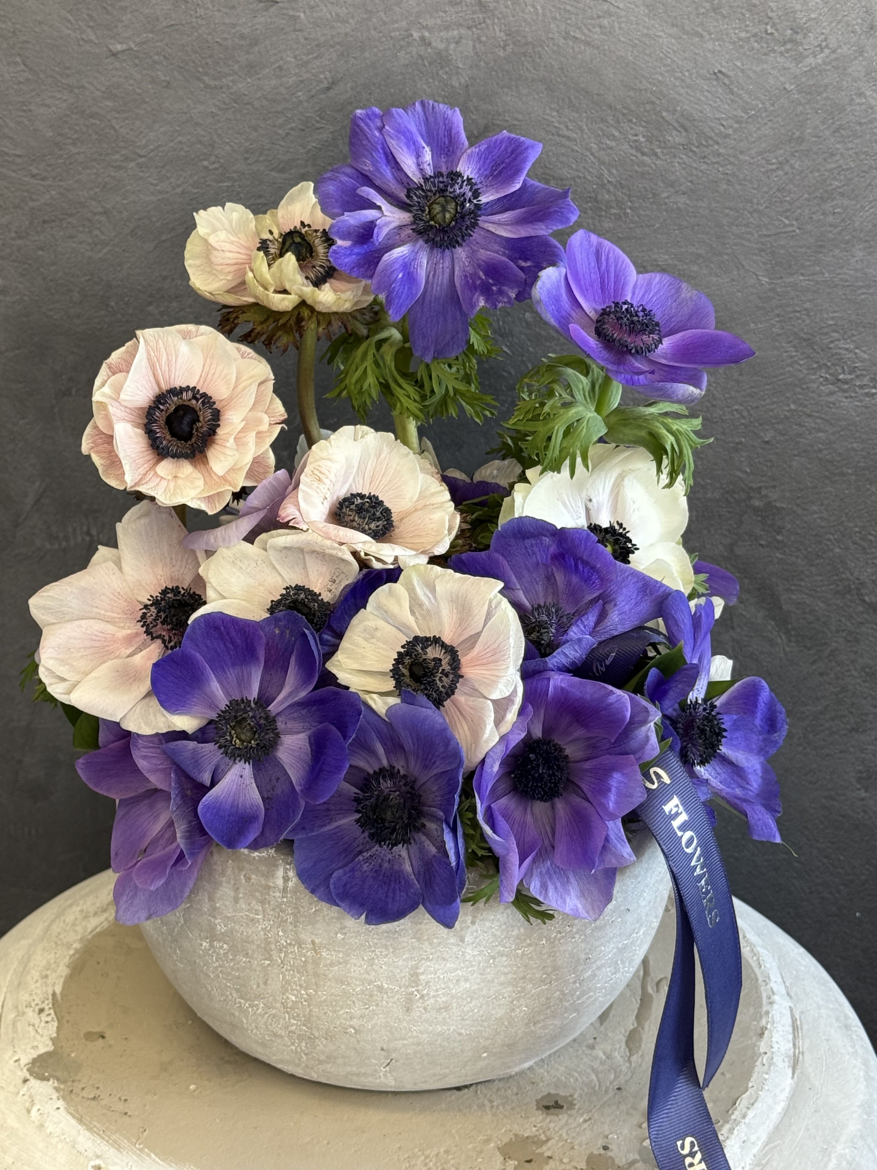 Purple and blush anemones arranged in a round white vase