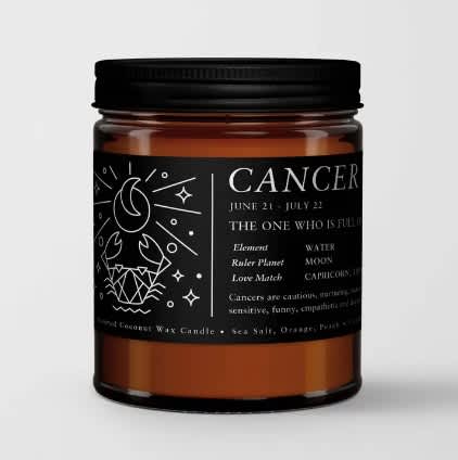 Amber jar candle with a black label reading Cancer