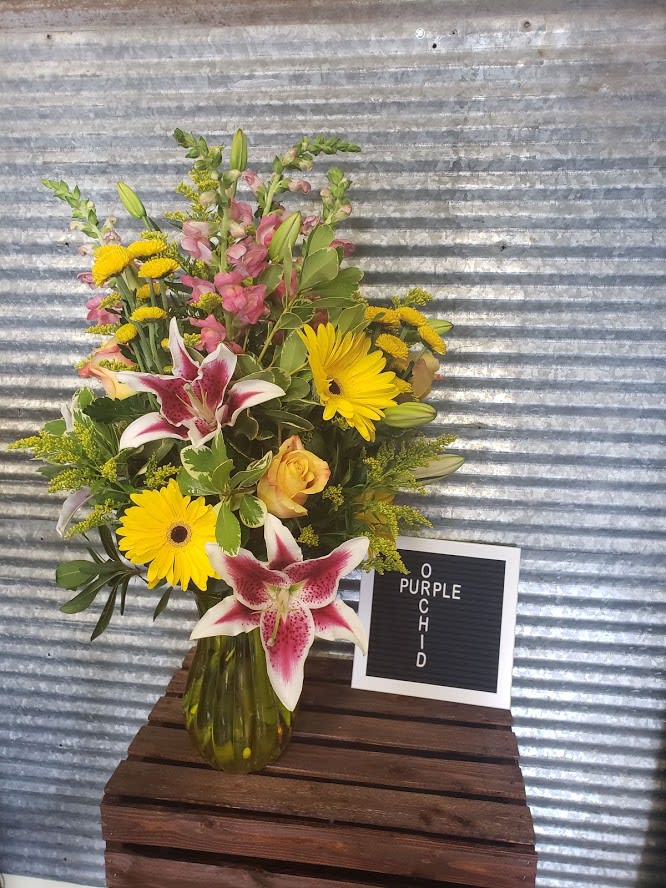 Mixed bouquet with yellow daisies, pink lilies, and roses in a glass vase
