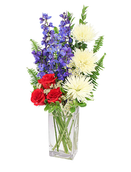 Red roses, purple flowers, and white blooms in a clear rectangular vase