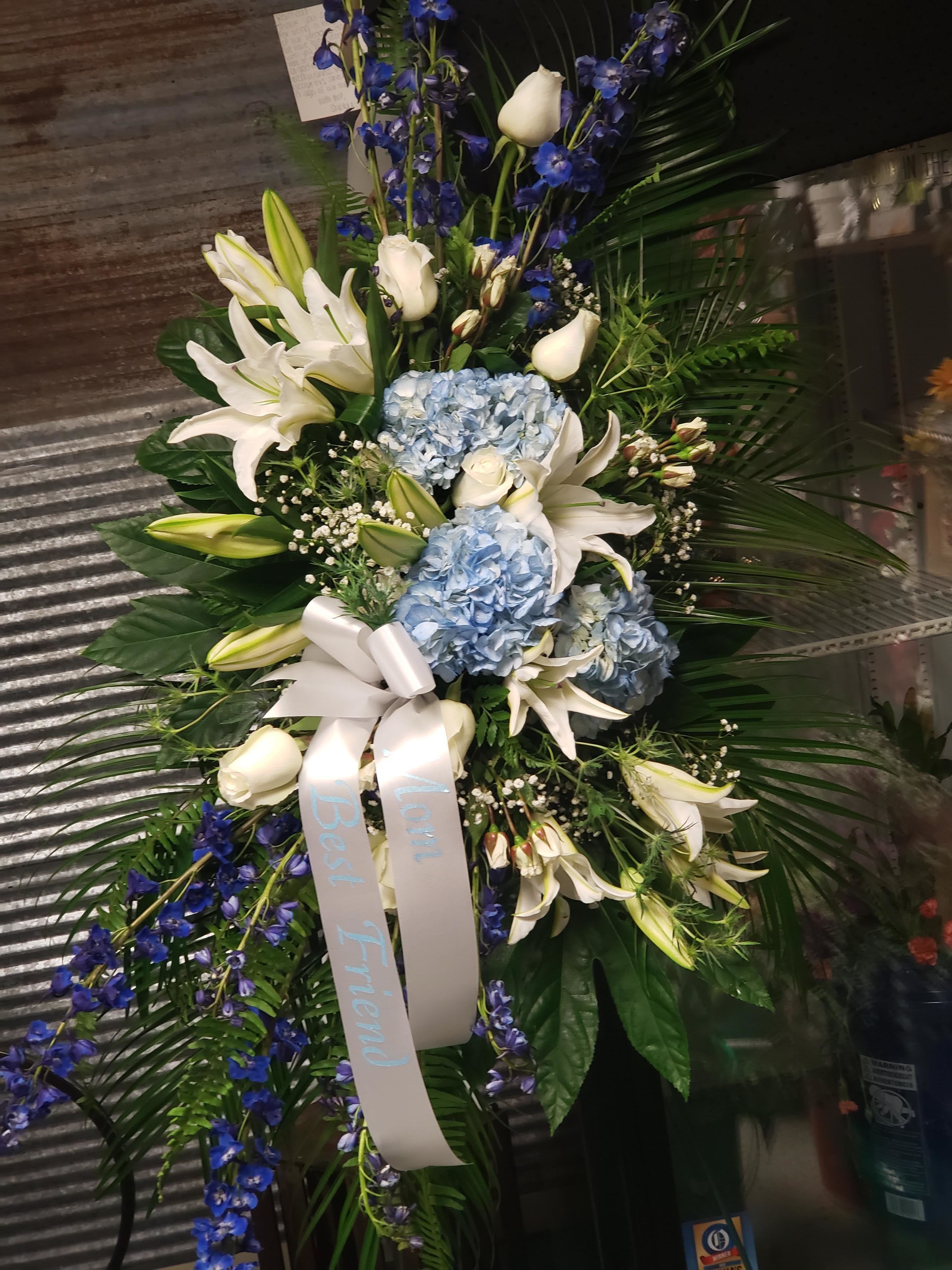 Standing floral spray with white lilies, blue hydrangeas, and blue ribbon