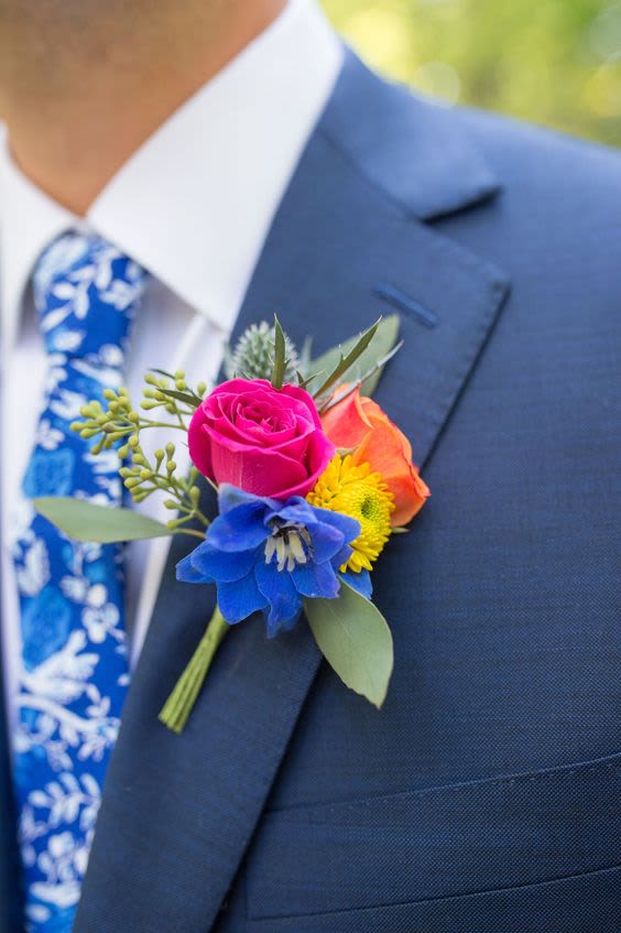 Colorful boutonniere with roses and a blue flower on a suit lapel