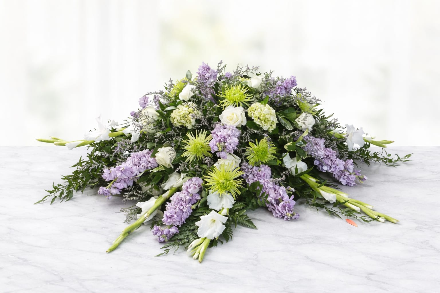 Serene Lavender Full Casket Spray - The Serene Lavender Full Casket Spray is a peaceful and elegant tribute designed to honor a life with grace and beauty. This full-length casket spray features soft lavender stock, white roses, green hydrangea, spider mums, snapdragons, and delicate accent flowers, finished with lush greenery for a natural, flowing presentation. Designed by an experienced Omaha florist, this arrangement offers a calming blend of lavender, white, and green tones and is appropriate for funeral and memorial services. Each spray is handcrafted with care and attention to detail. Details Style: full casket spray Color palette: lavender, white, soft green Design: garden-inspired, flowing, and serene Suitable for closed or open casket services Flower varieties may vary slightly based on seasonal availability while maintaining the overall color palette and fullness.