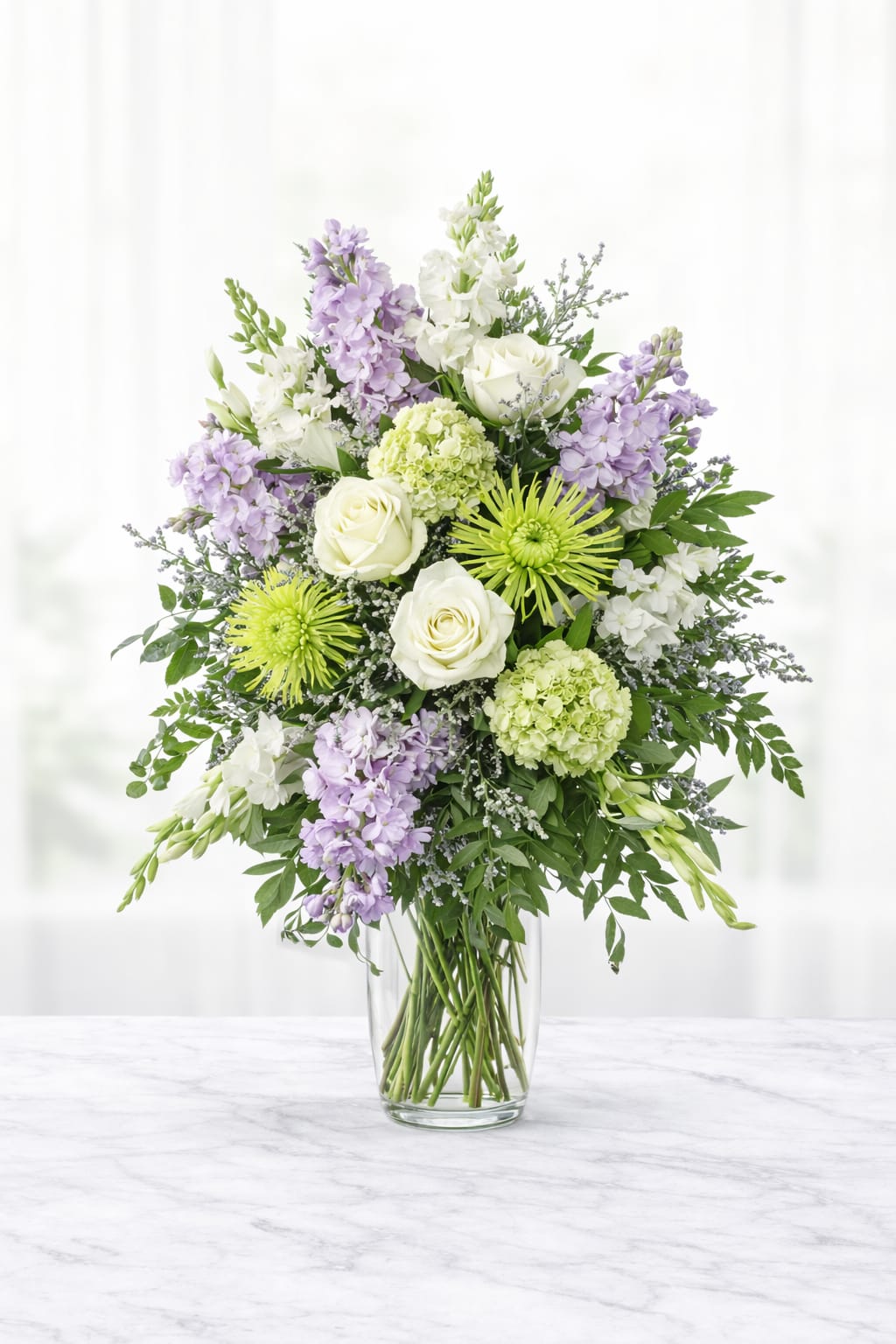 Serene Lavender Vase - The Serene Lavender is an elegant vase arrangement features soft lavender stock, white roses, green hydrangea, spider mums, snapdragons, and delicate seasonal accents, finished with lush greenery for a natural, flowing look. Handcrafted by an experienced Omaha florist, this design offers a soothing palette of lavender, white, and soft green tones, making it a thoughtful expression of sympathy for the home, Birthday, Anniversary or Just because. Details Style:  vase arrangement Color palette: lavender, white, soft green Design: garden-inspired, full, and elegant Coordinates also with the Serene Lavender Sympathy Collection Flower varieties may vary slightly based on seasonal availability while maintaining the overall color palette and fullness.