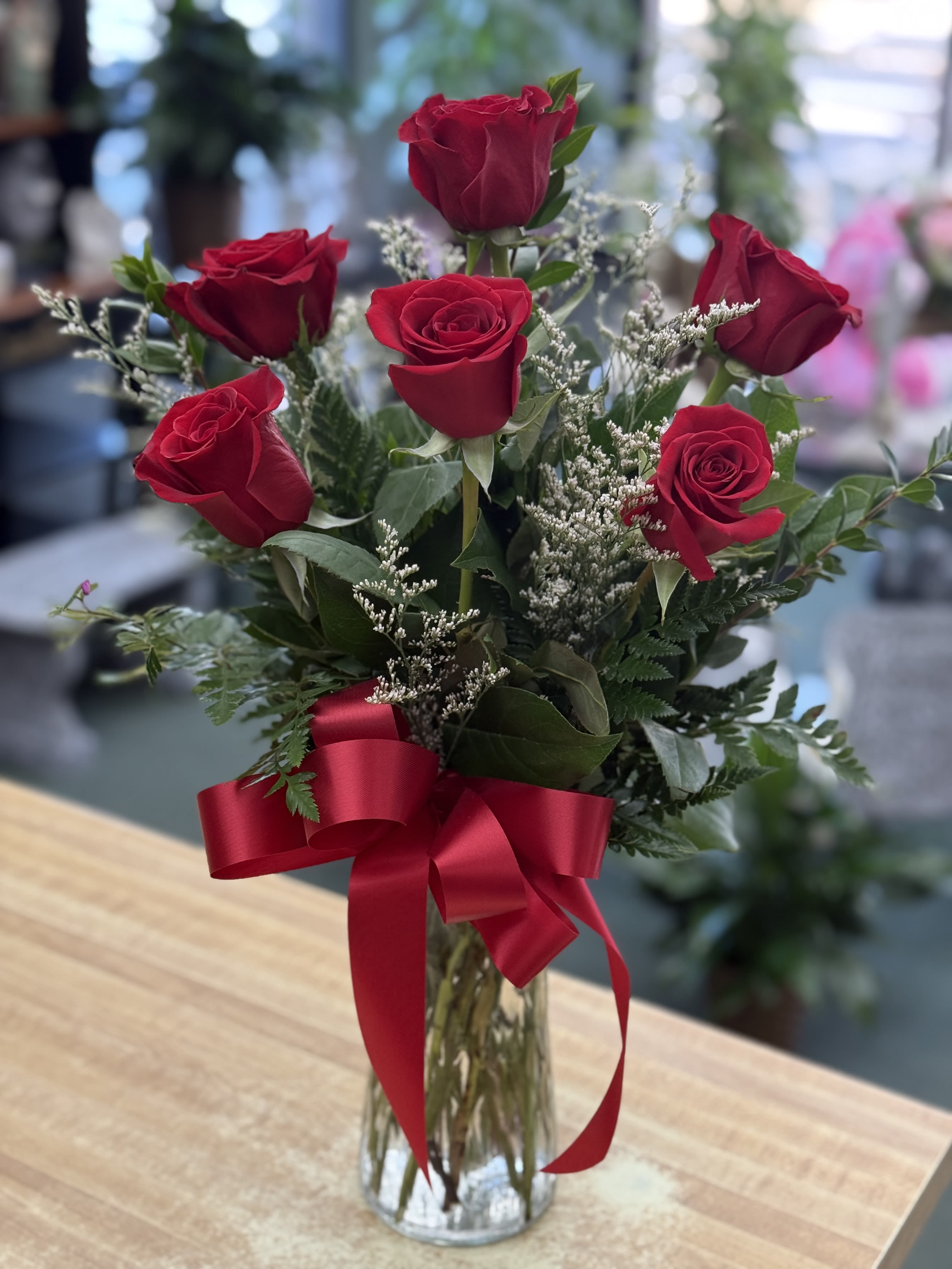Red roses arranged in a clear glass vase with a red ribbon