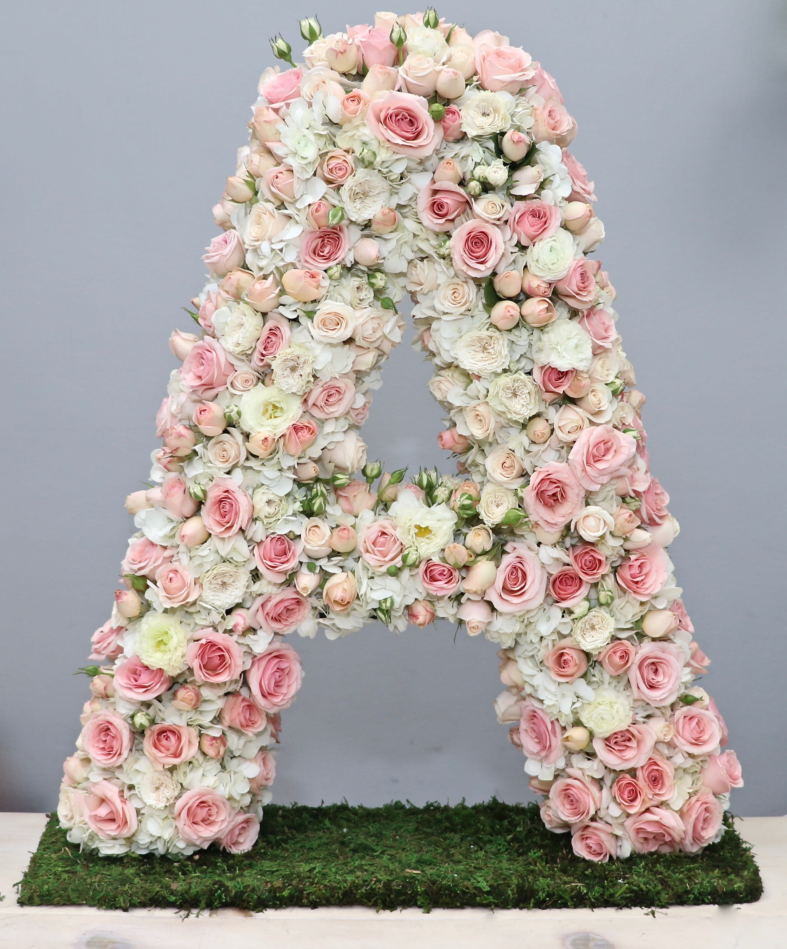 Tall floral letter A made of soft pink and white roses and hydrangeas on a moss-covered base