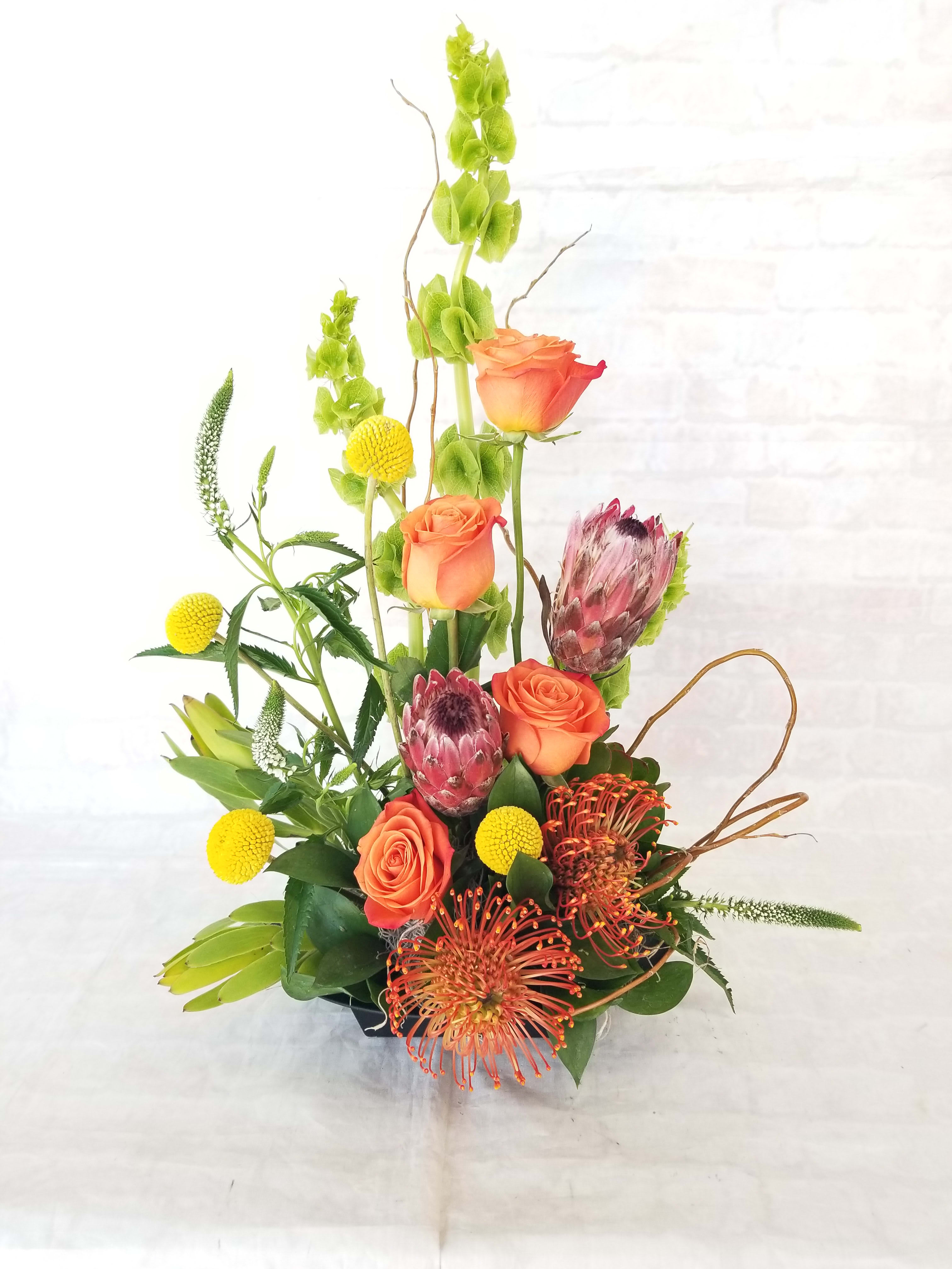 Tall mixed bouquet with orange roses, protea, and yellow accents in a vase