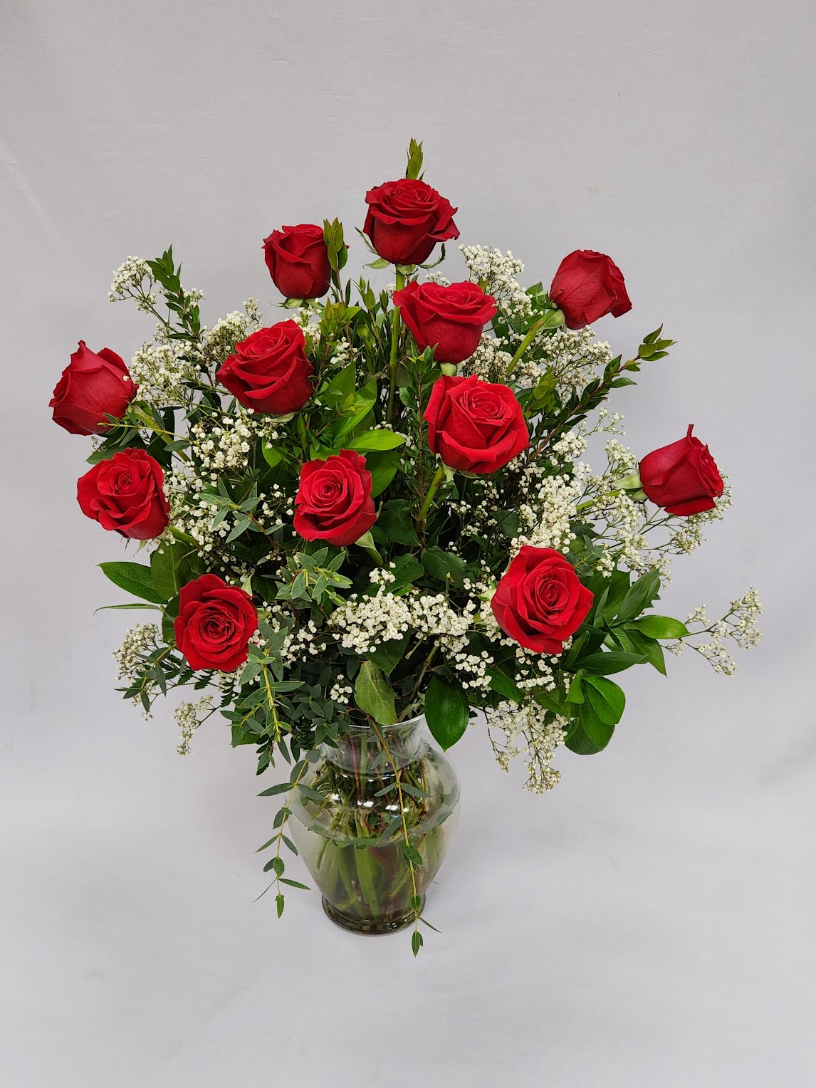 Red roses arranged in a clear glass vase with white filler flowers