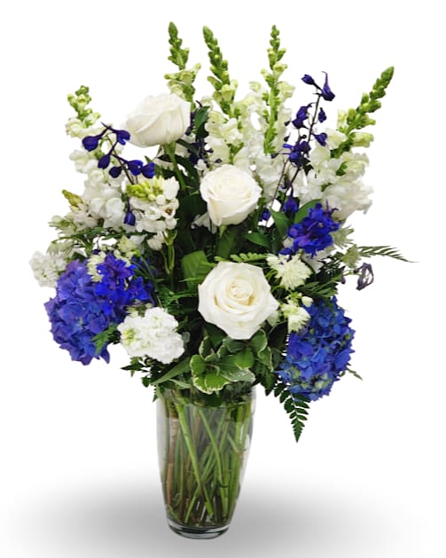 Blue Elegance - Blue Elegance is a graceful arrangement designed in a clear glass vase with a refined mix of white and blue blooms. Featuring rich blue hydrangea, elegant white roses, striking delphinium, snapdragons, and lush greenery, this design brings a timeless sense of beauty and sophistication. Perfect for both celebrations and moments of remembrance, it offers a classic expression of style and grace.