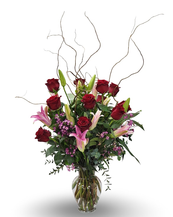 Red roses and pink lilies in a clear glass vase with curly branches