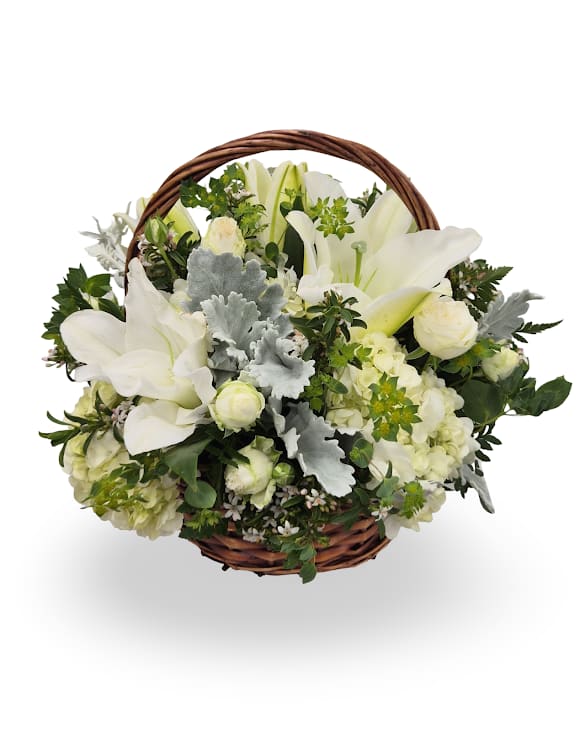White lilies and roses arranged in a round wicker basket with handle