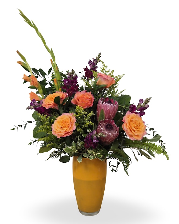 Sunset Dream - Sunset Dreams features glowing sunset-toned blooms in peach, coral, and golden yellow with lush greenery, arranged in a textured yellow keepsake vase for a warm golden-hour feel.   Approx. 34" x 12"