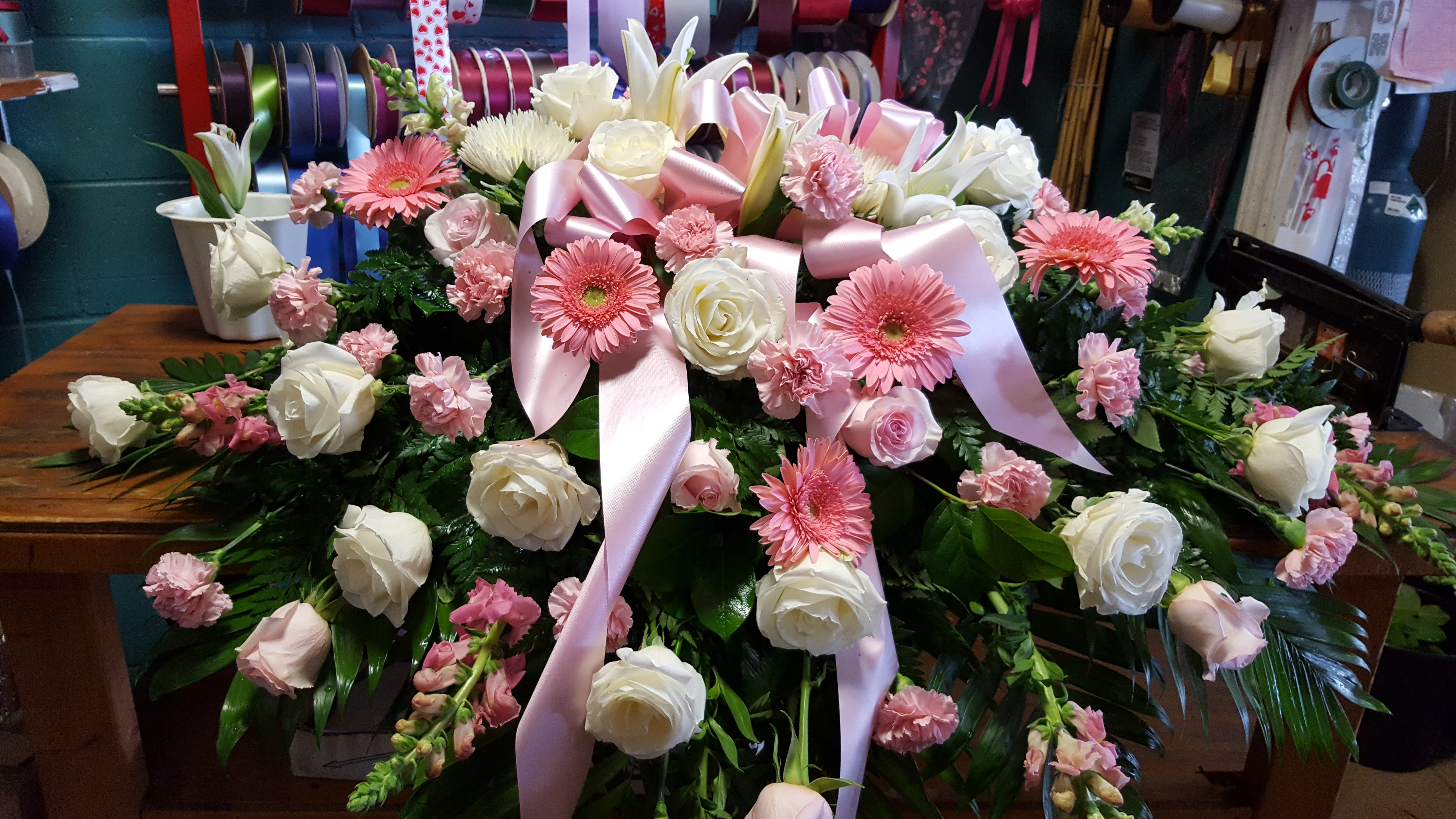 Pink and white floral casket spray with ribbon accents