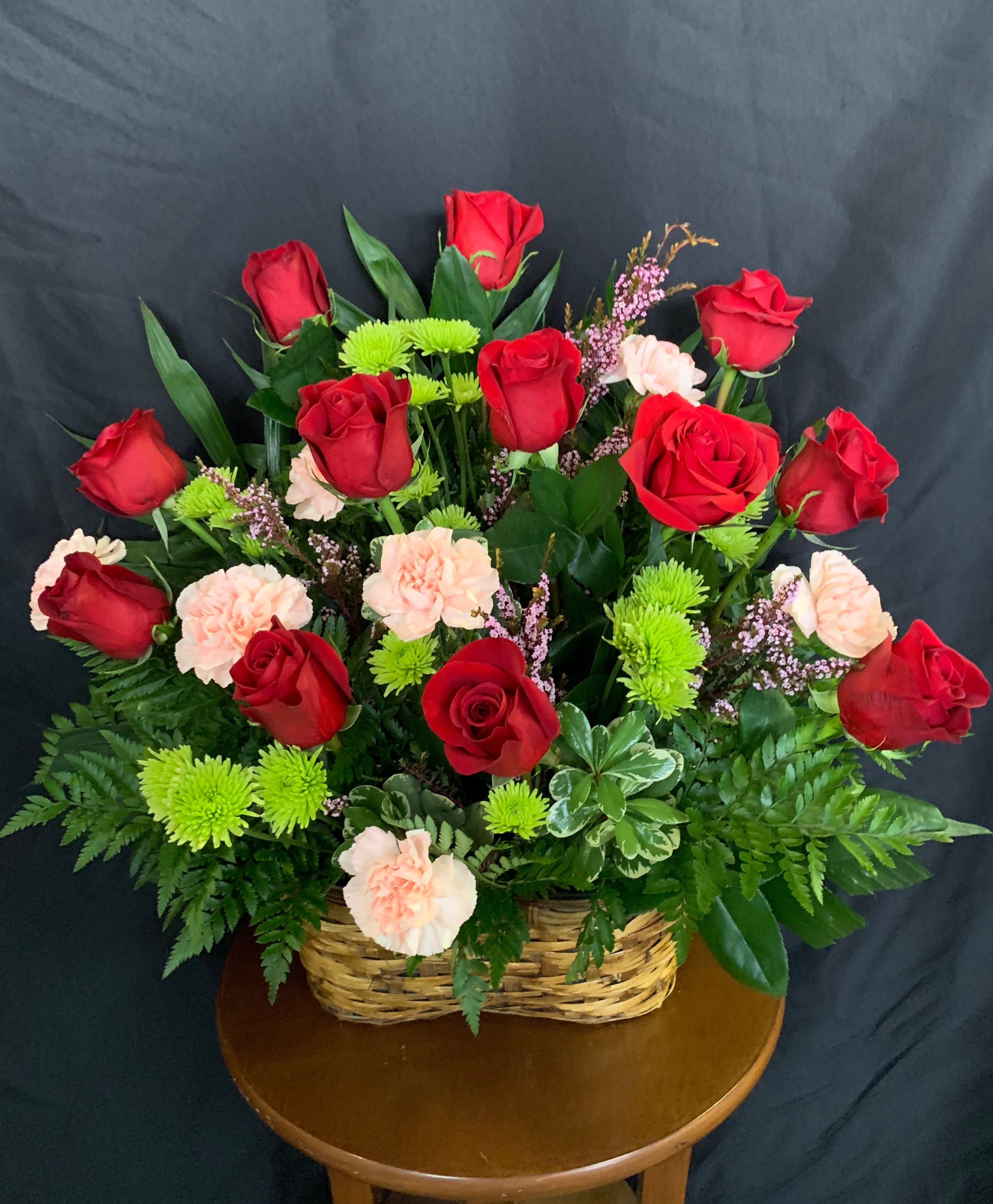 Basket arrangement of red roses, pale pink carnations, and green mums