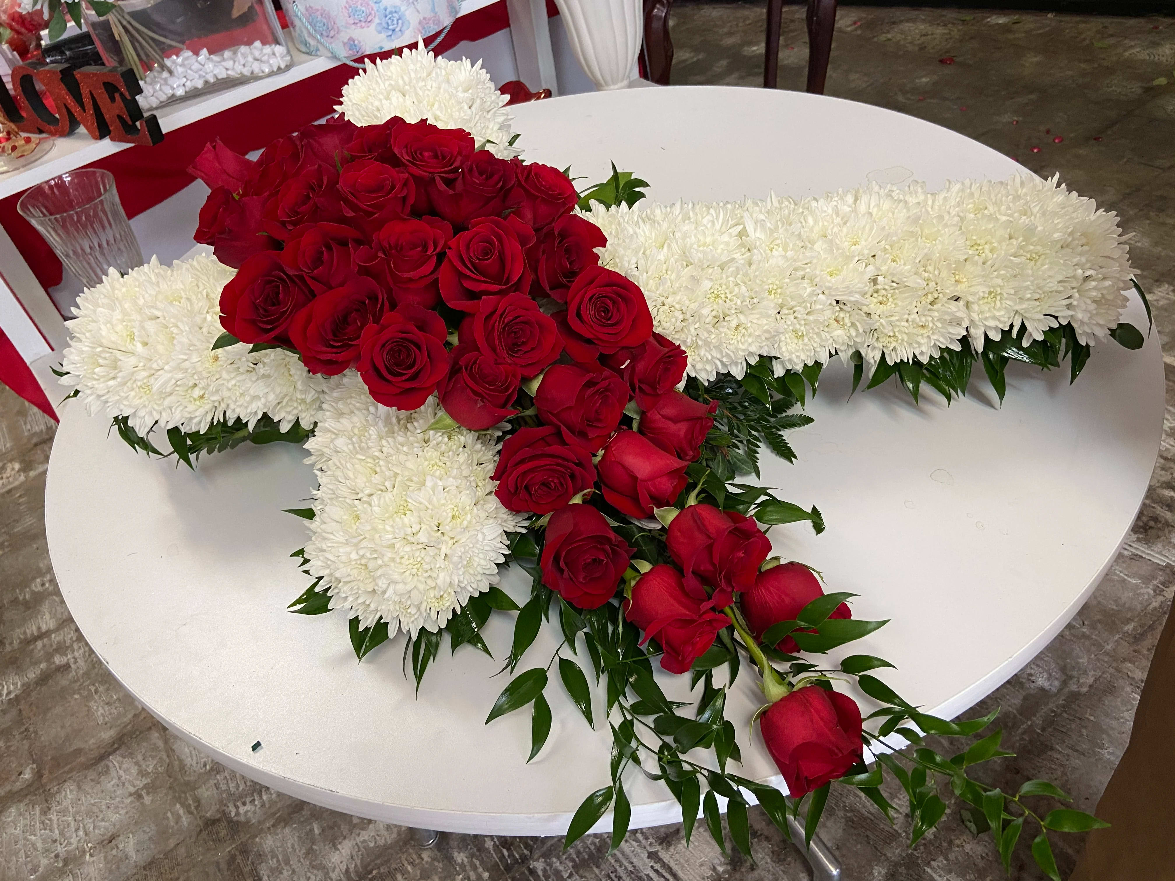 Red roses arranged over a white cross-shaped floral tribute