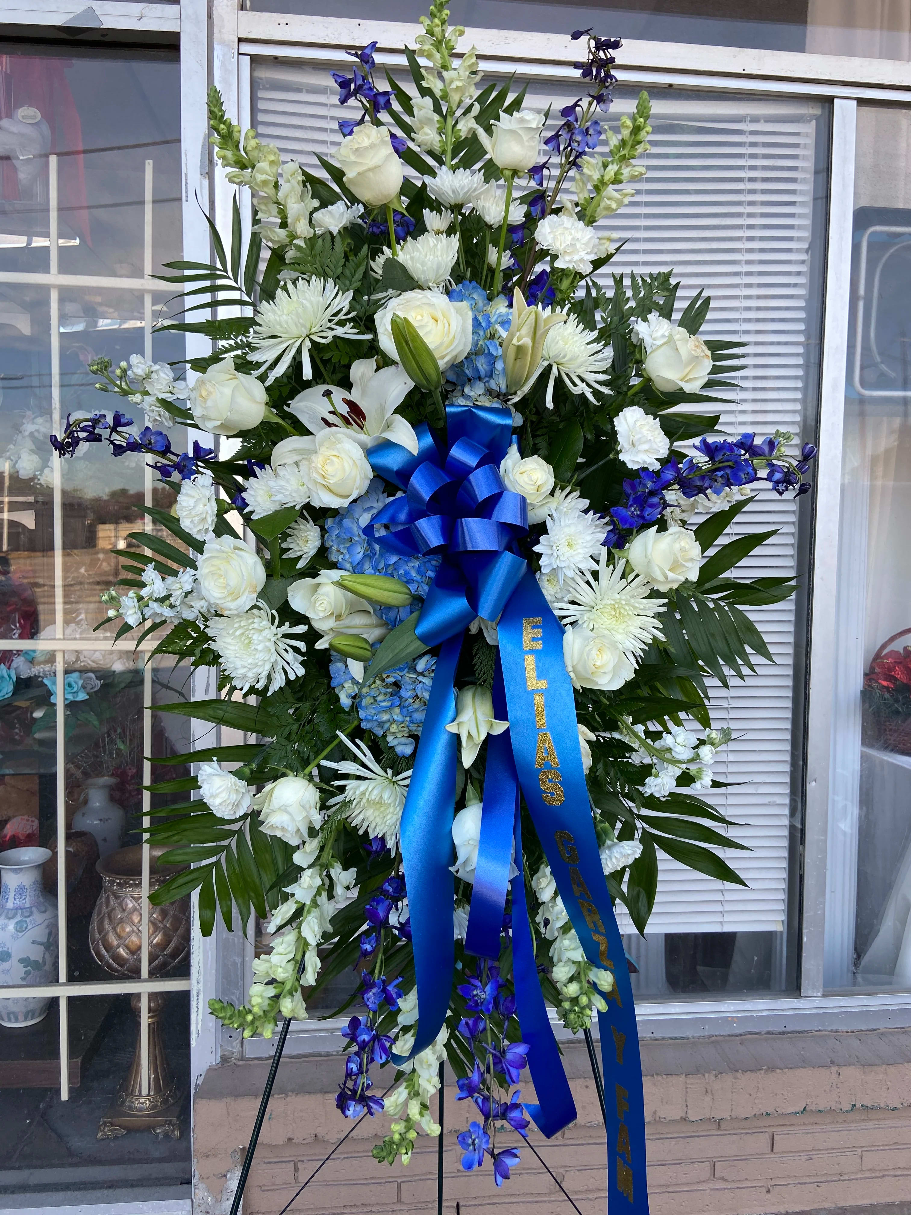 Tall white and blue funeral spray on an easel with a blue ribbon