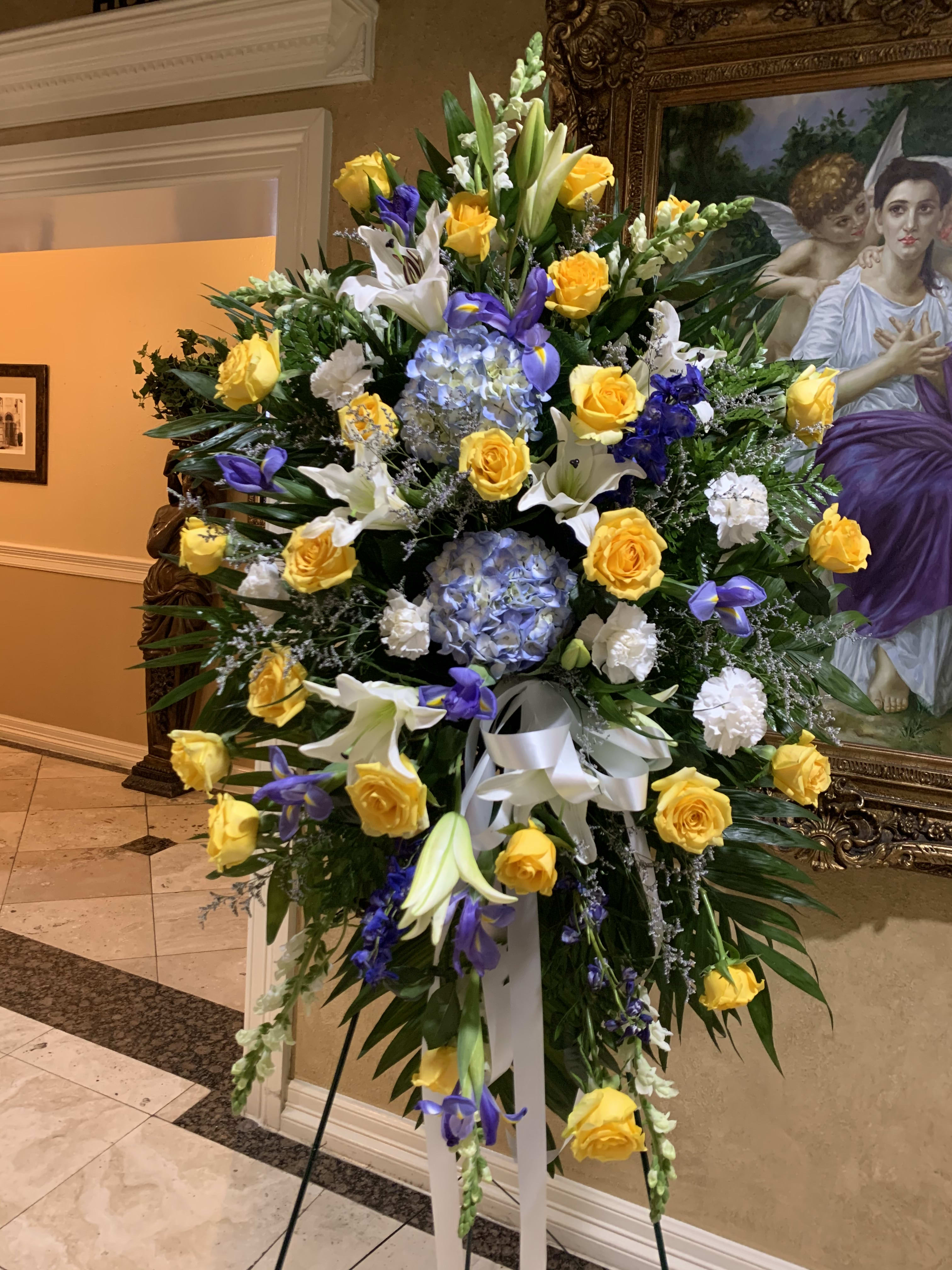 Large standing floral spray with yellow roses, white lilies, and purple blooms