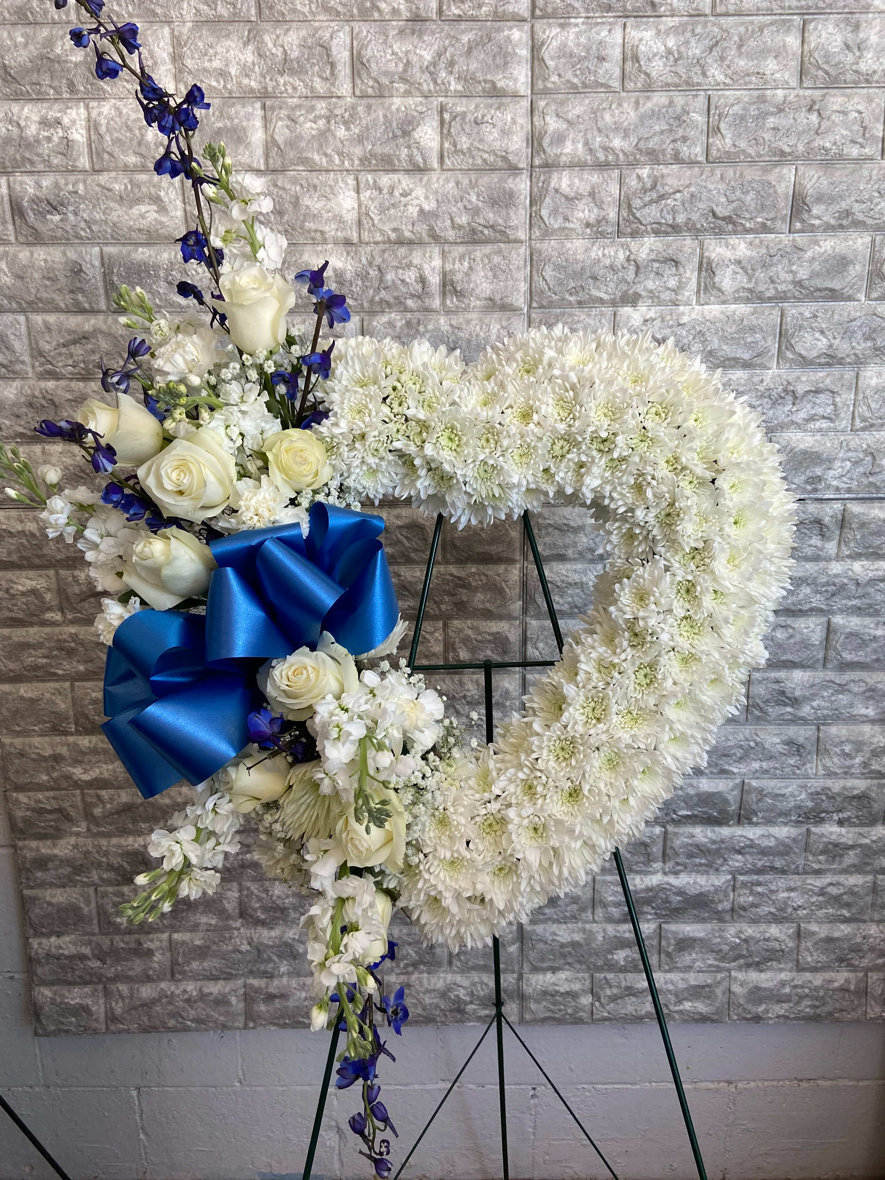 White floral heart wreath with blue ribbon on a stand