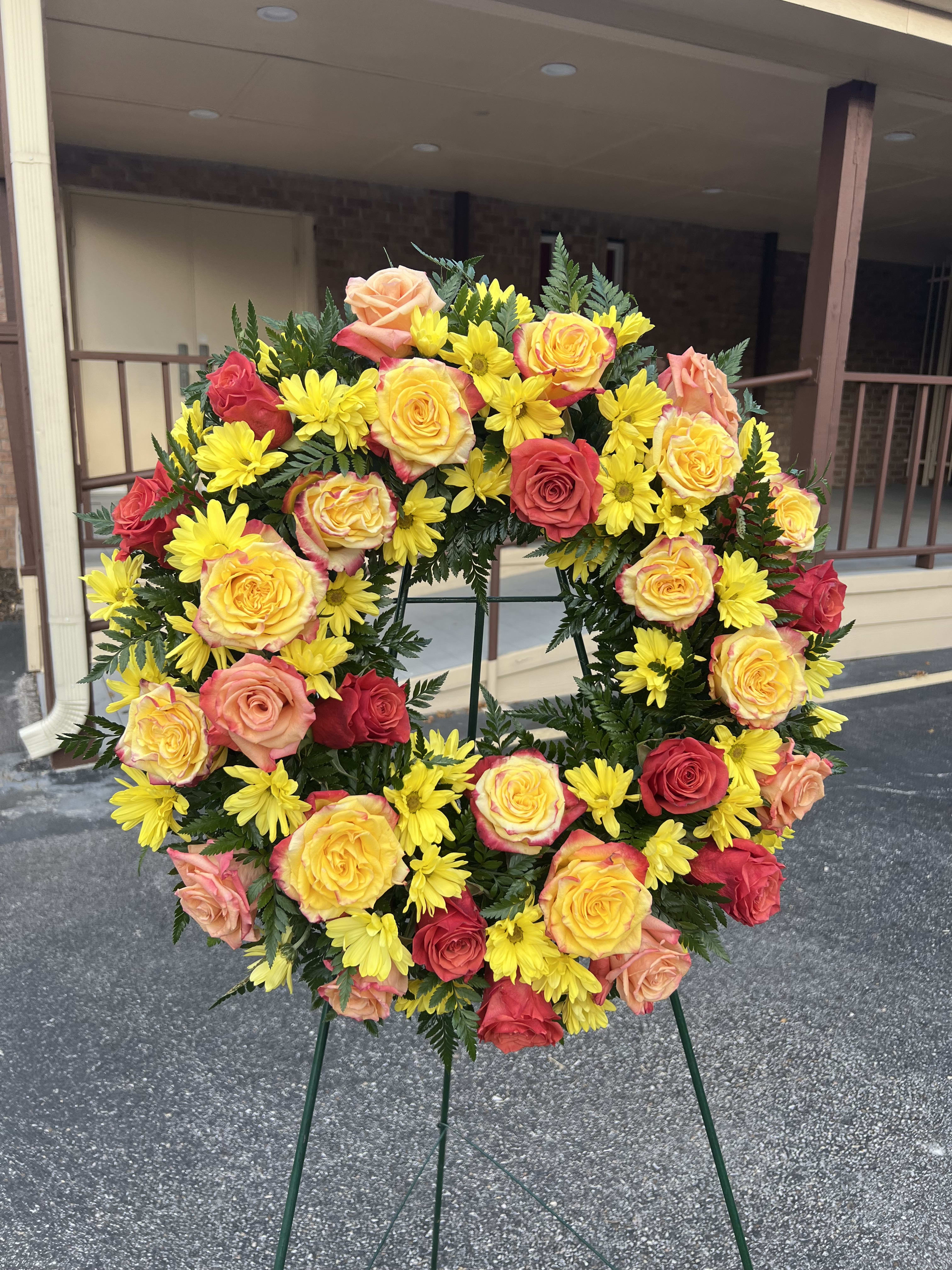 Circular wreath of yellow daisies and multicolored roses on a stand