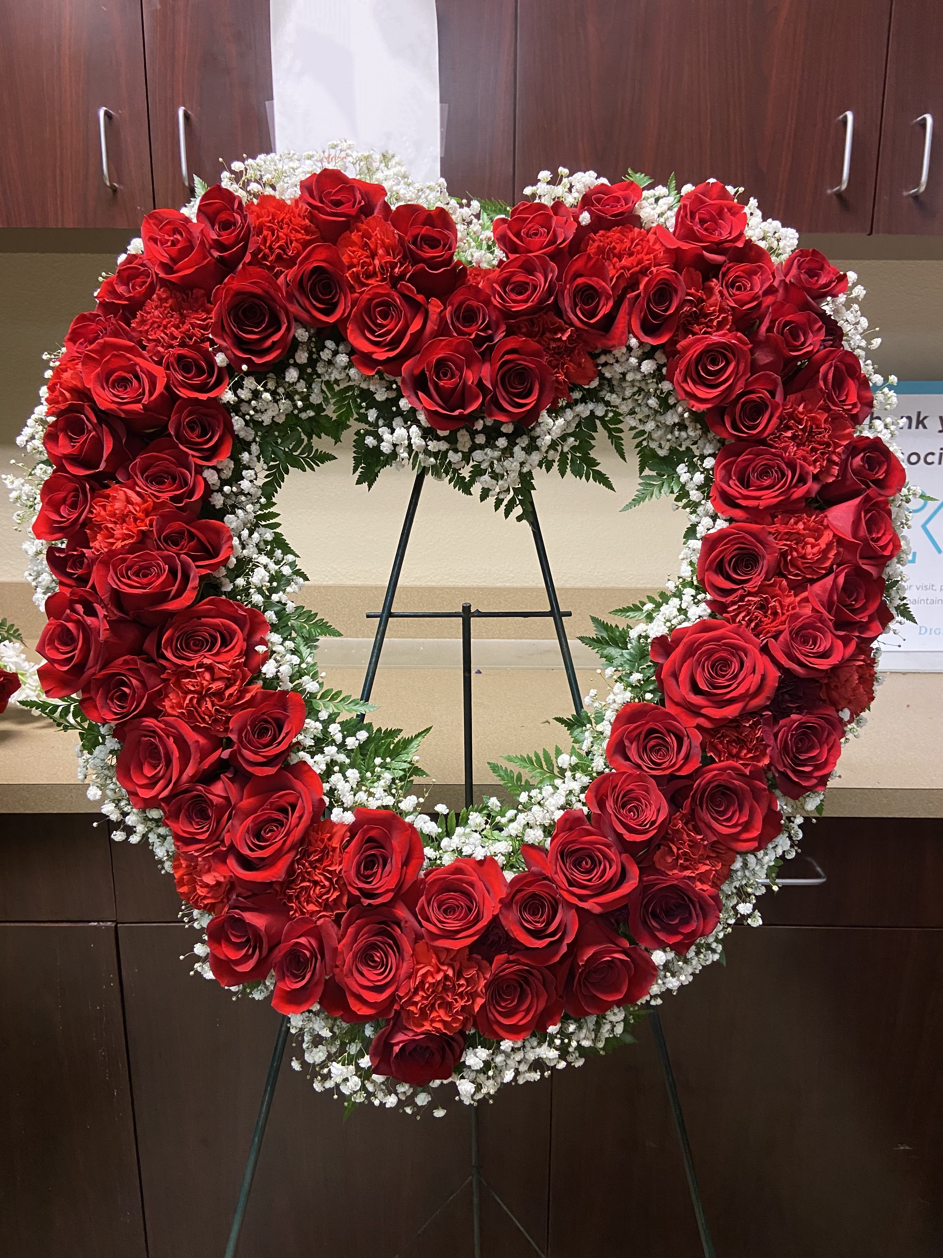 Heart-shaped red rose wreath on a stand with white filler flowers