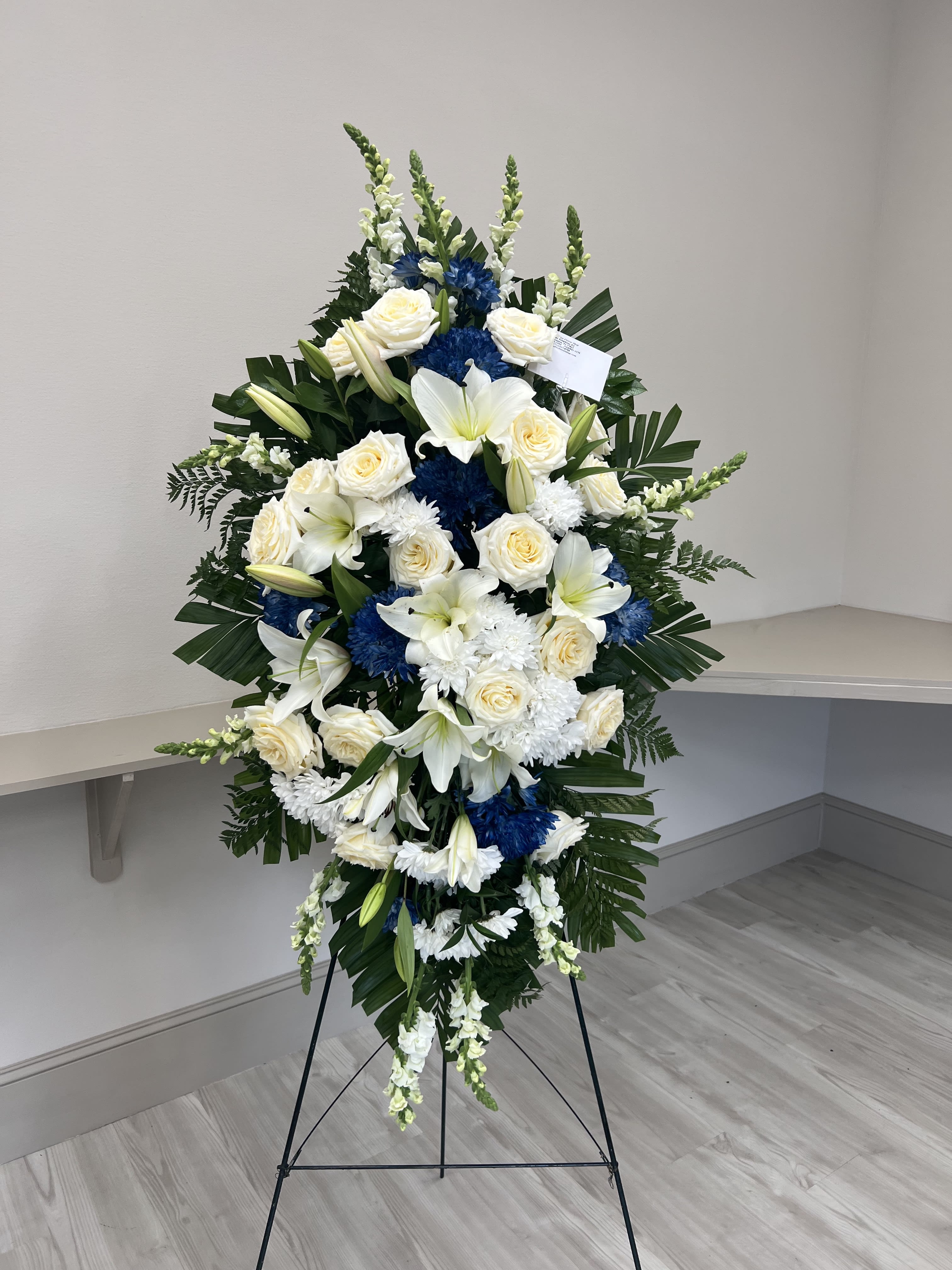 Standing floral spray with white roses, lilies, and blue chrysanthemums on an easel